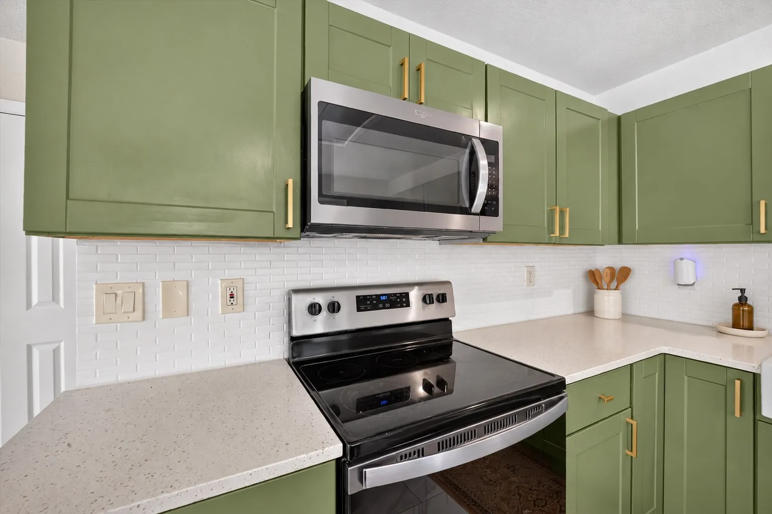 Kitchen featuring sage green cabinetry with gold-tone hardware, stainless steel appliances, a white subway tile backsplash, and light-toned countertops