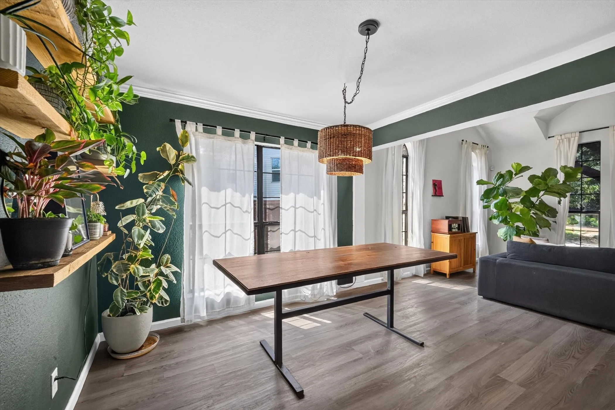 Wood-finish flooring, accent wall, crown molding, double-tiered woven pendant light fixture, and multiple large windows