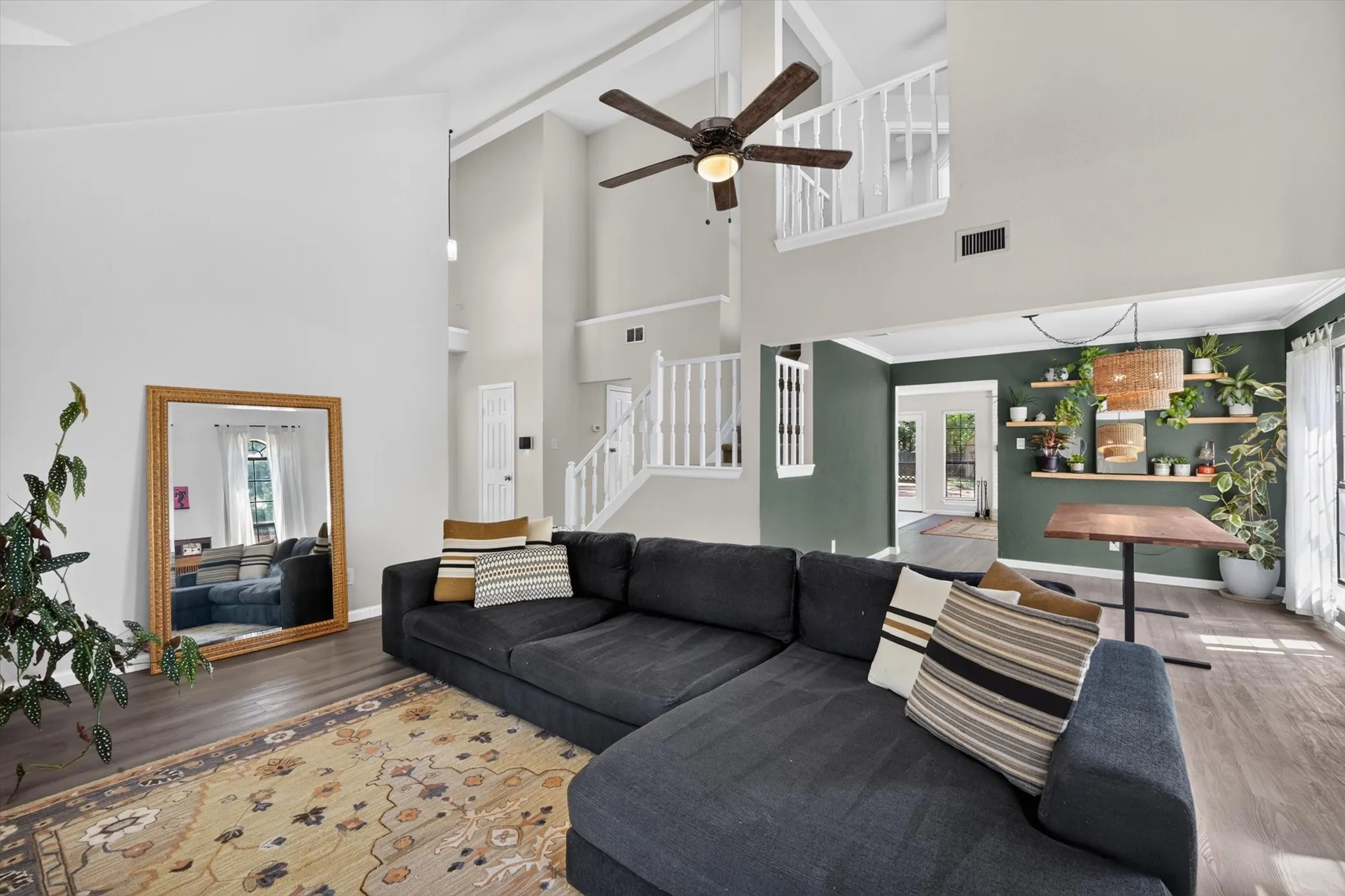 Living space with wood-finish flooring, a vaulted ceiling, a ceiling fan, and a built-in wall unit with shelving