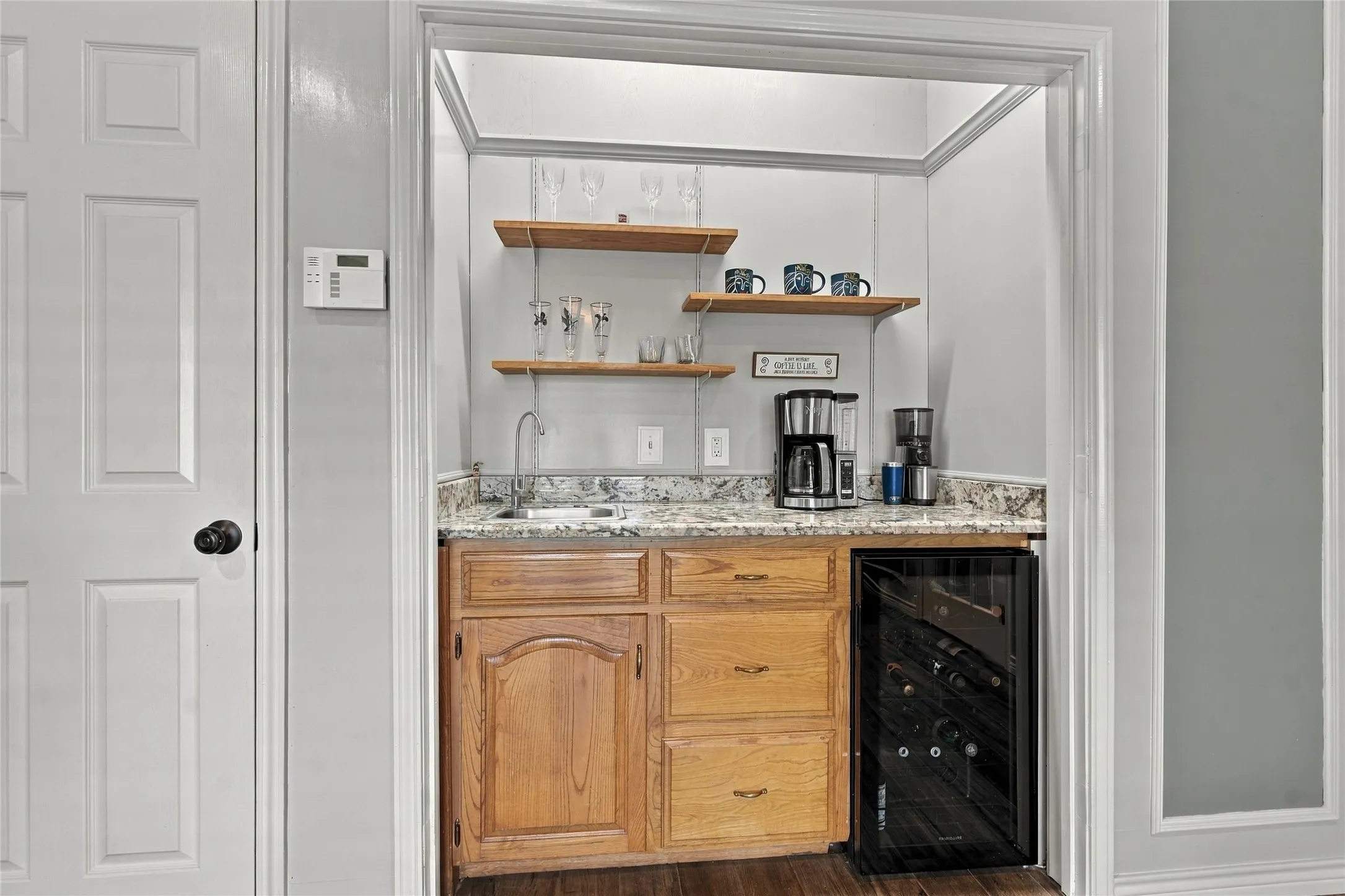 Built-in wet bar featuring a stainless steel sink, wood-finish cabinetry, and a beverage refrigerator
