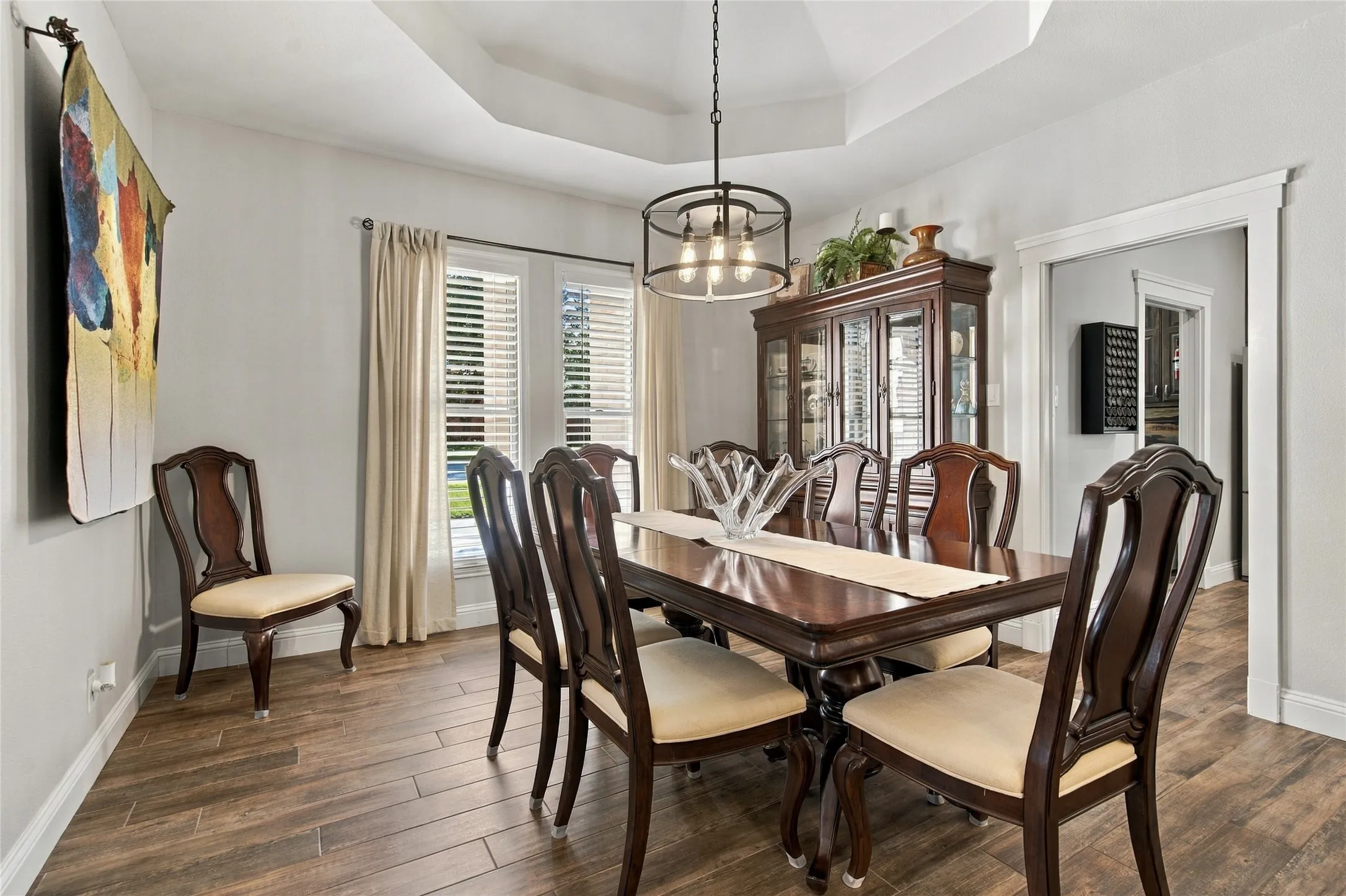 Tray ceiling with a suspended chandelier, wood-finish flooring, white trim, and a window with blinds