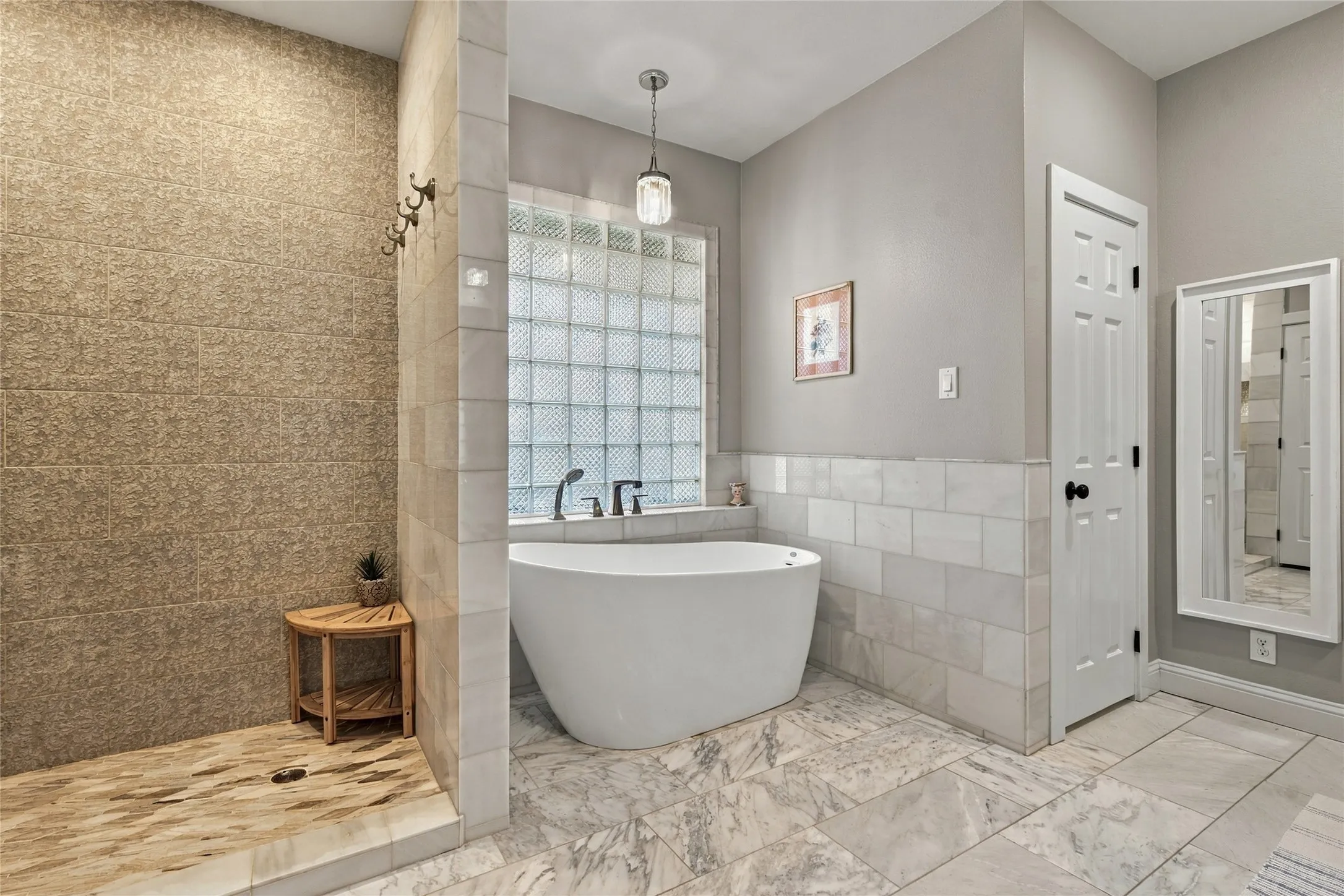 Freestanding soaking tub with a wall-mounted faucet, glass block window, and a tiled shower with a coordinating floor