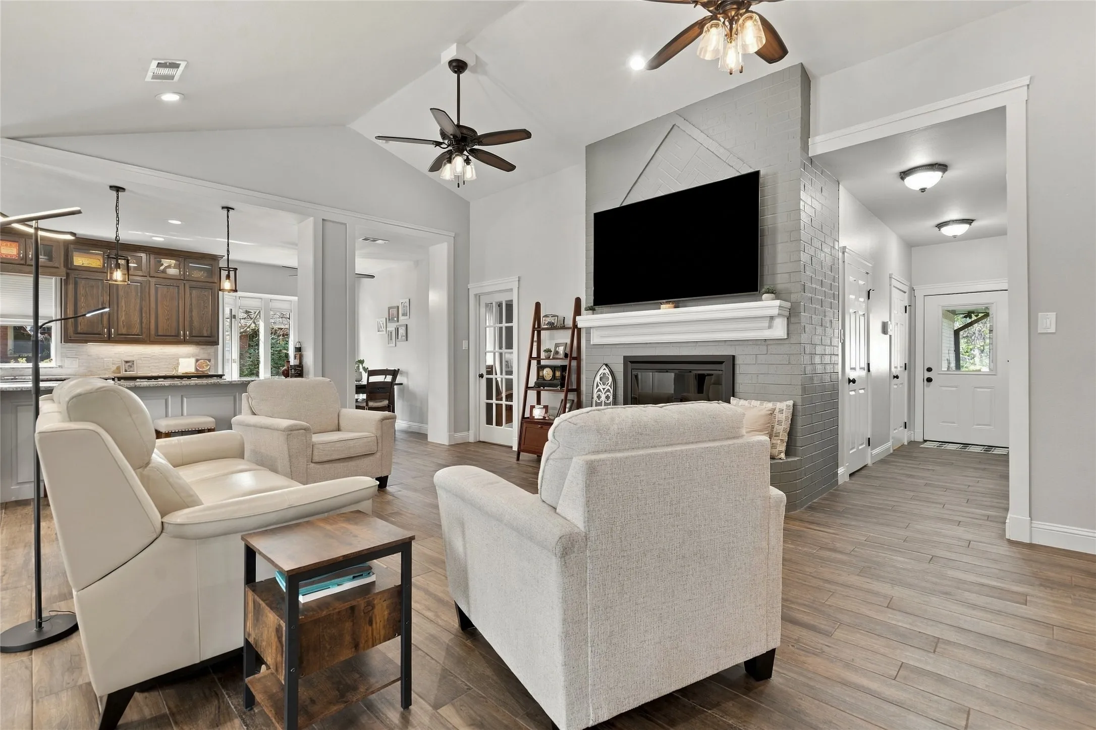 Vaulted ceiling with dual ceiling fans, wood-finish flooring, and a fireplace with a gray tile surround