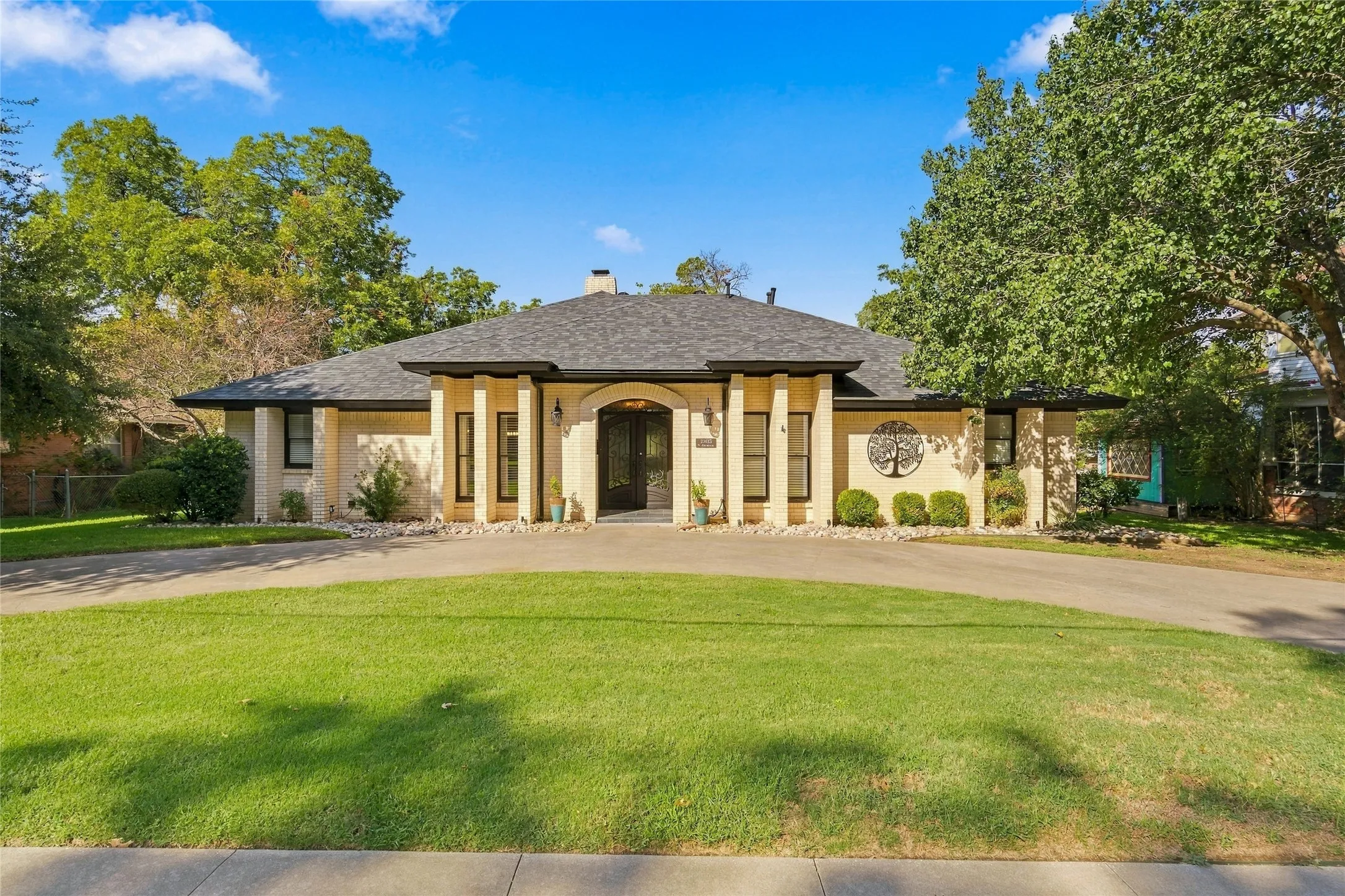 Semicircular driveway with a manicured lawn, stucco exterior, dark roof, arched entry, and decorative metal wall art