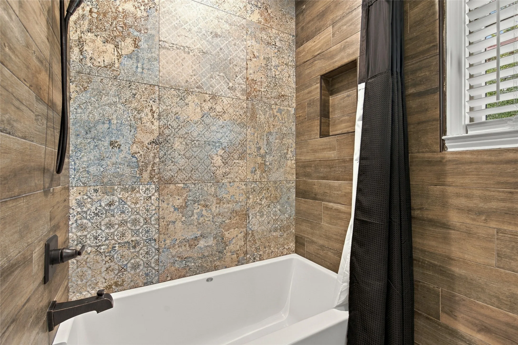 Freestanding tub with oil-rubbed bronze fixtures, decorative wall tiling, wood-finish tile accents, and a built-in shower niche