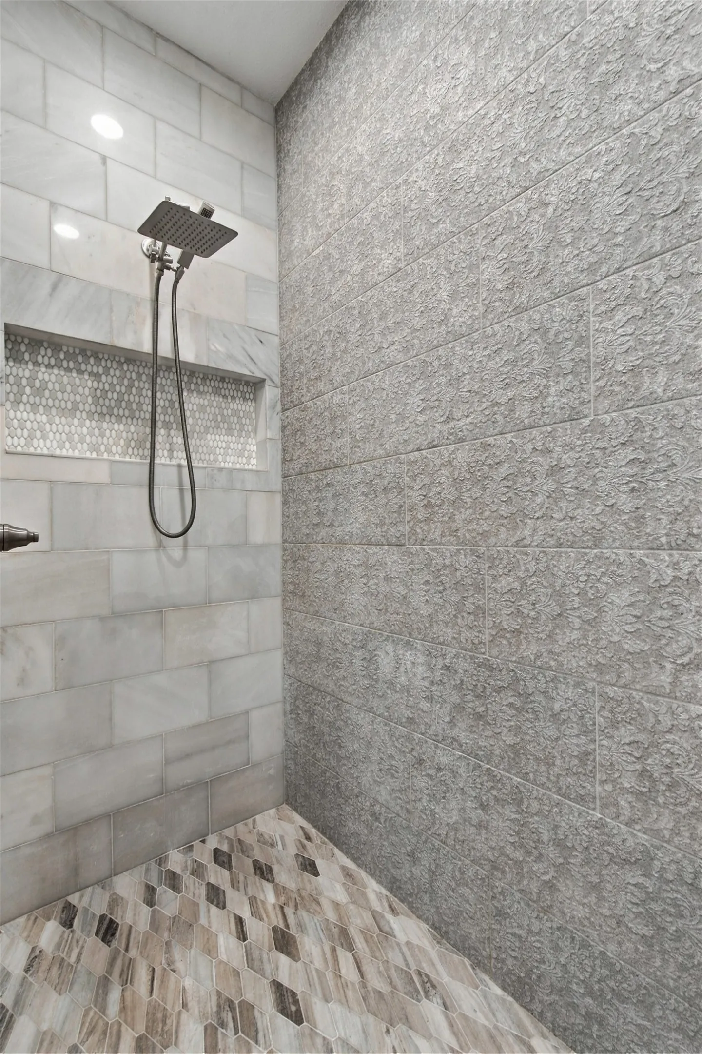 Shower with a rainfall showerhead, rectangular wall niche with mosaic tile, large format wall tiles, and patterned floor tiles