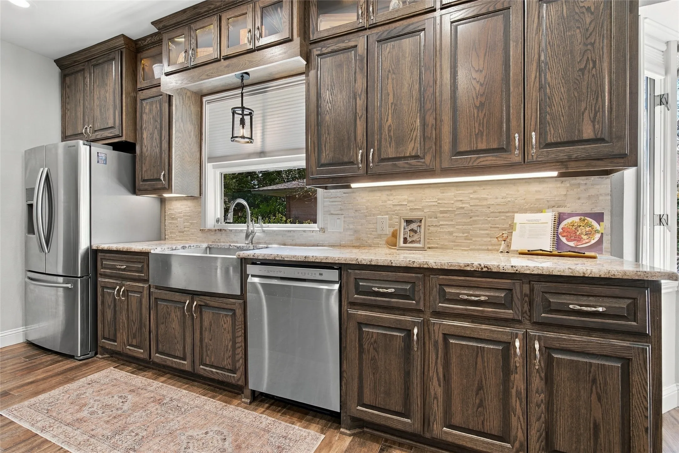 Kitchen featuring dark wood cabinetry, stainless steel appliances, a farmhouse sink, stone countertops, and a tiled backsplash