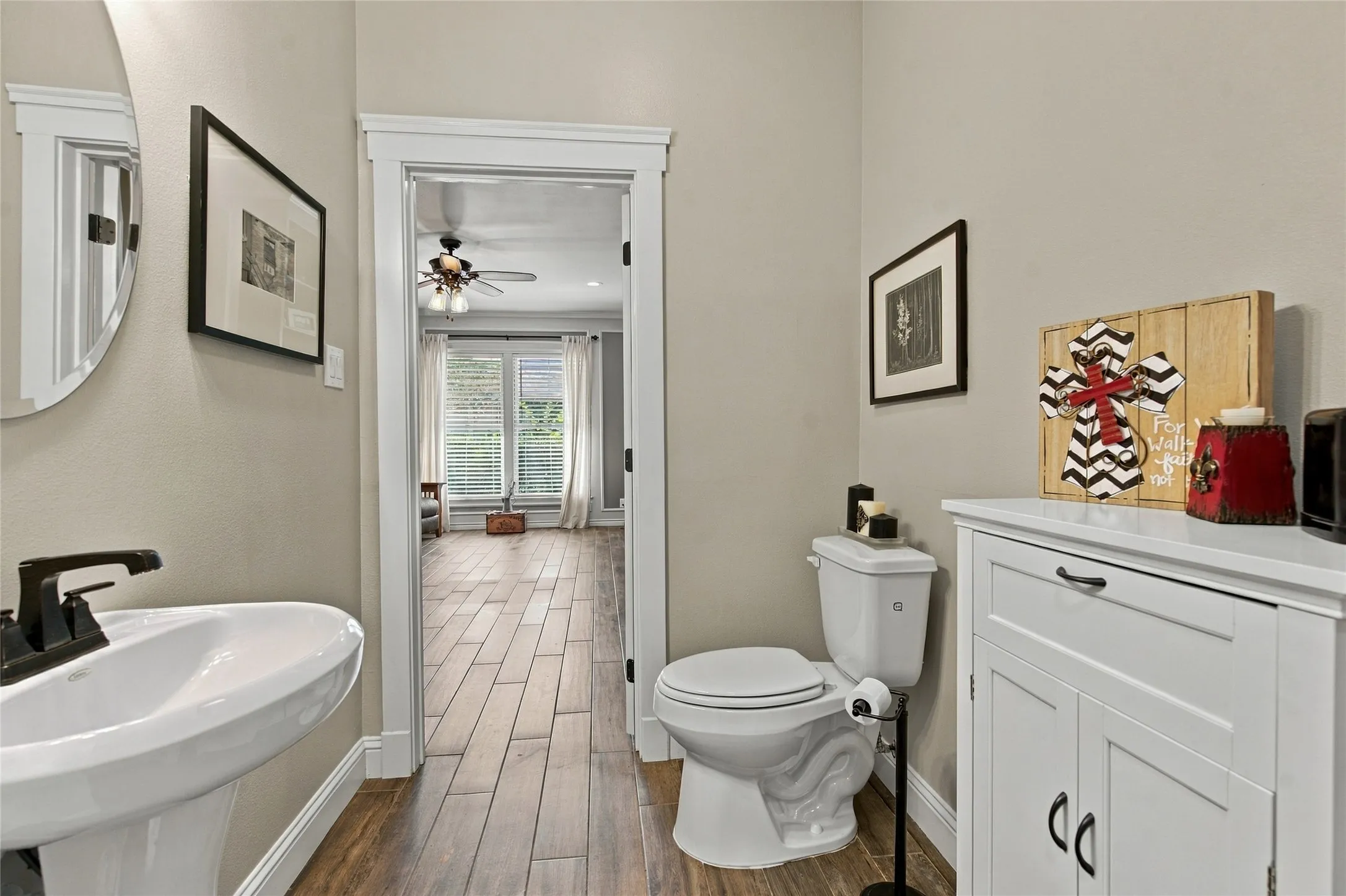 Pedestal sink with dark bronze faucet, wood-finish flooring, white vanity with dark bronze hardware, white toilet, and recessed lighting