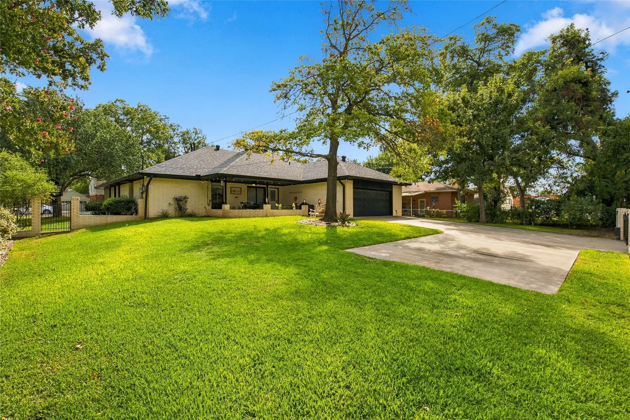 Expansive front lawn with mature trees, a paved driveway, and a two-car garage