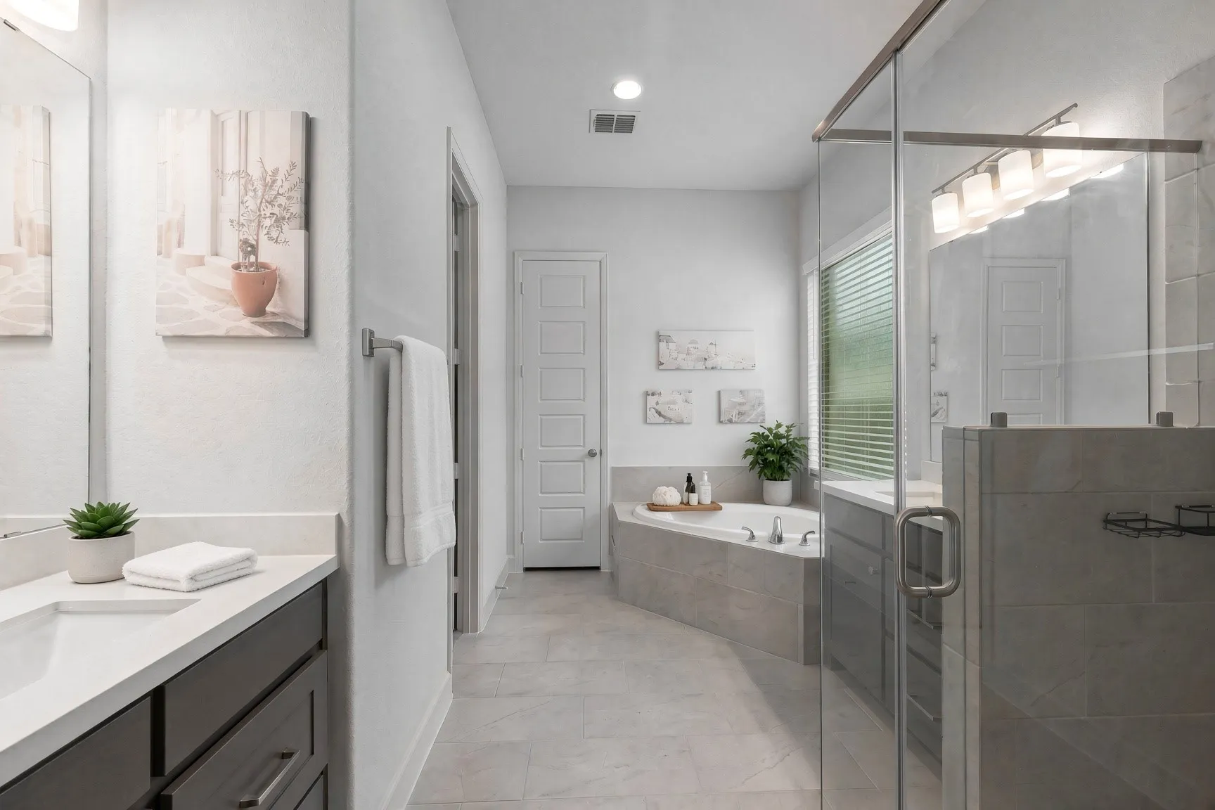 Bathroom featuring a built-in corner bathtub, a glass-enclosed shower, a vanity with a white countertop and integrated sink, and gray floor tiling