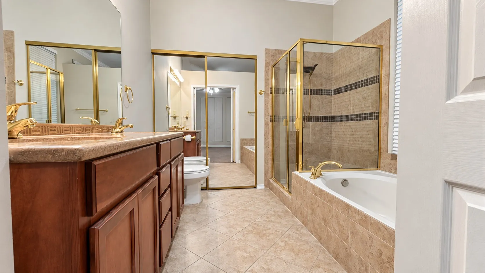 Dual wood-finish vanity with countertop, tiled flooring, built-in soaking tub, and enclosed shower with tile surround
