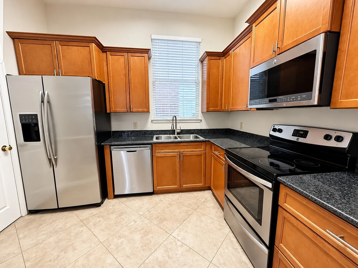 Kitchen featuring wood cabinetry, dark countertops, stainless steel appliances, and tile flooring