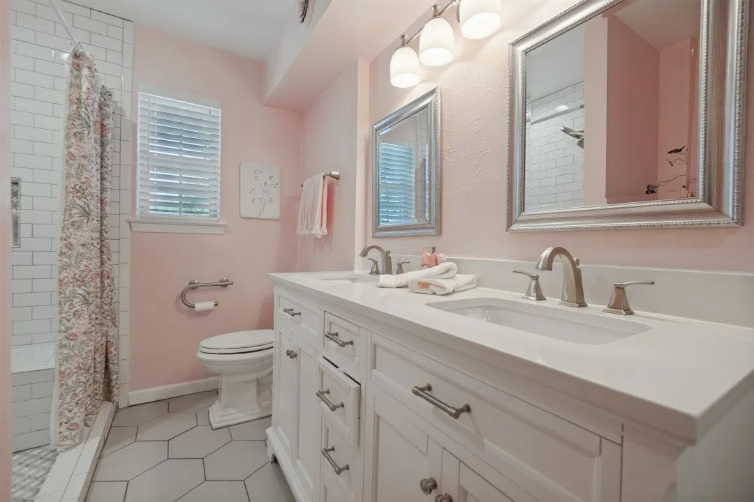 Primary Bathroom has remodeled vanity with double sinks, quartz countertop, recent hardware, comfort-height toilet, grab-bar toilet paper holder, handicap accessible shower with bench & grab bars, updated tile flooring.