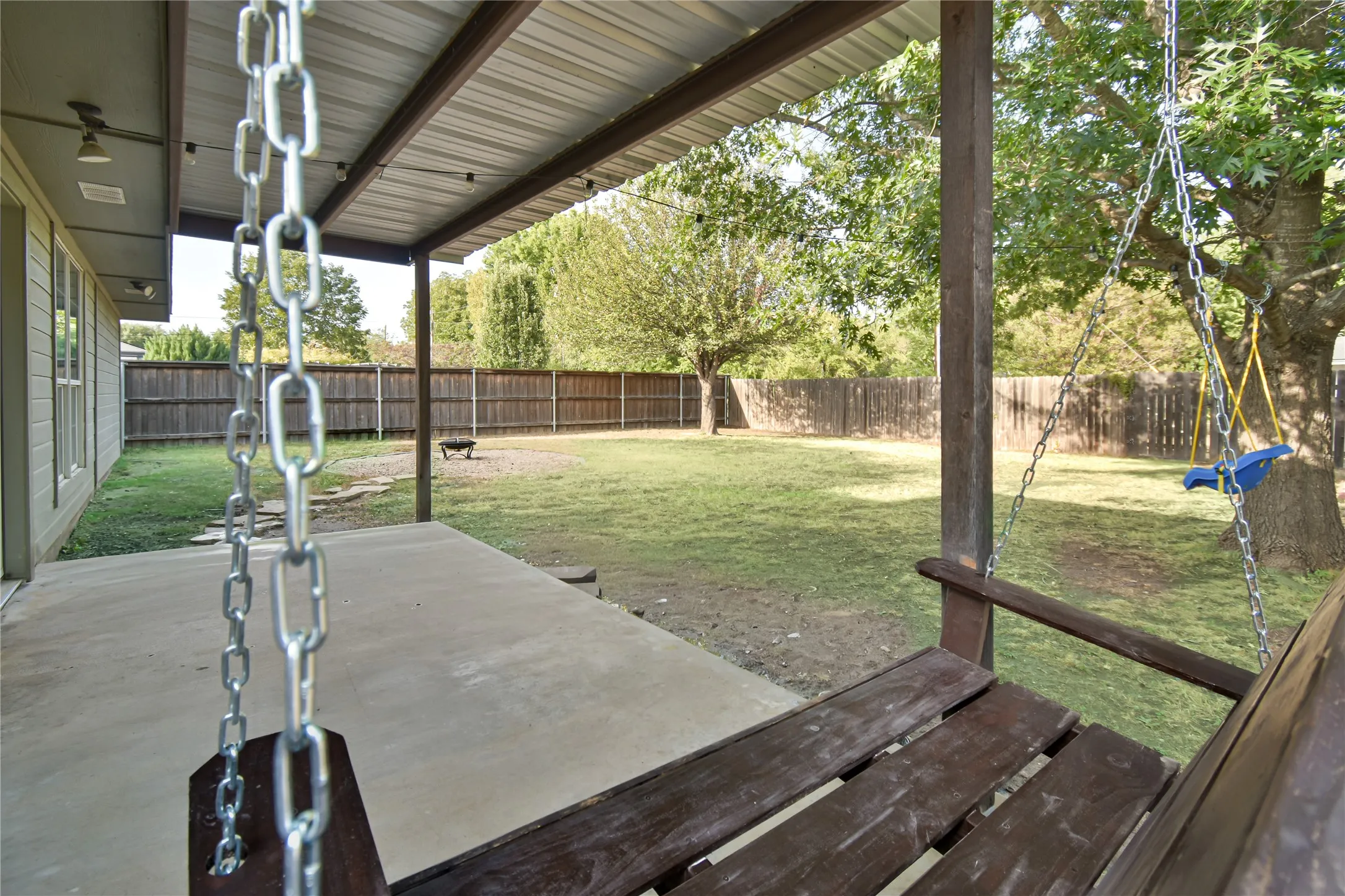 Covered patio with concrete flooring, wood privacy fencing, and mature trees