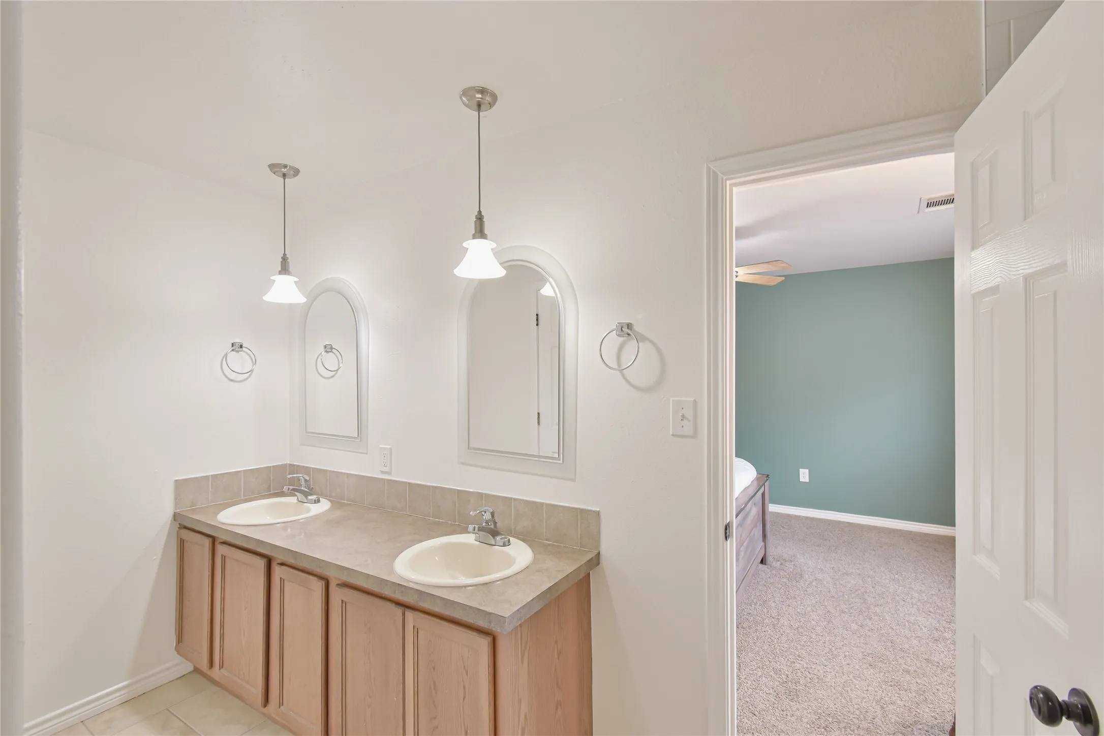 Double vanity with neutral countertop and integrated sinks, accented by pendant lighting and individual arched mirrors