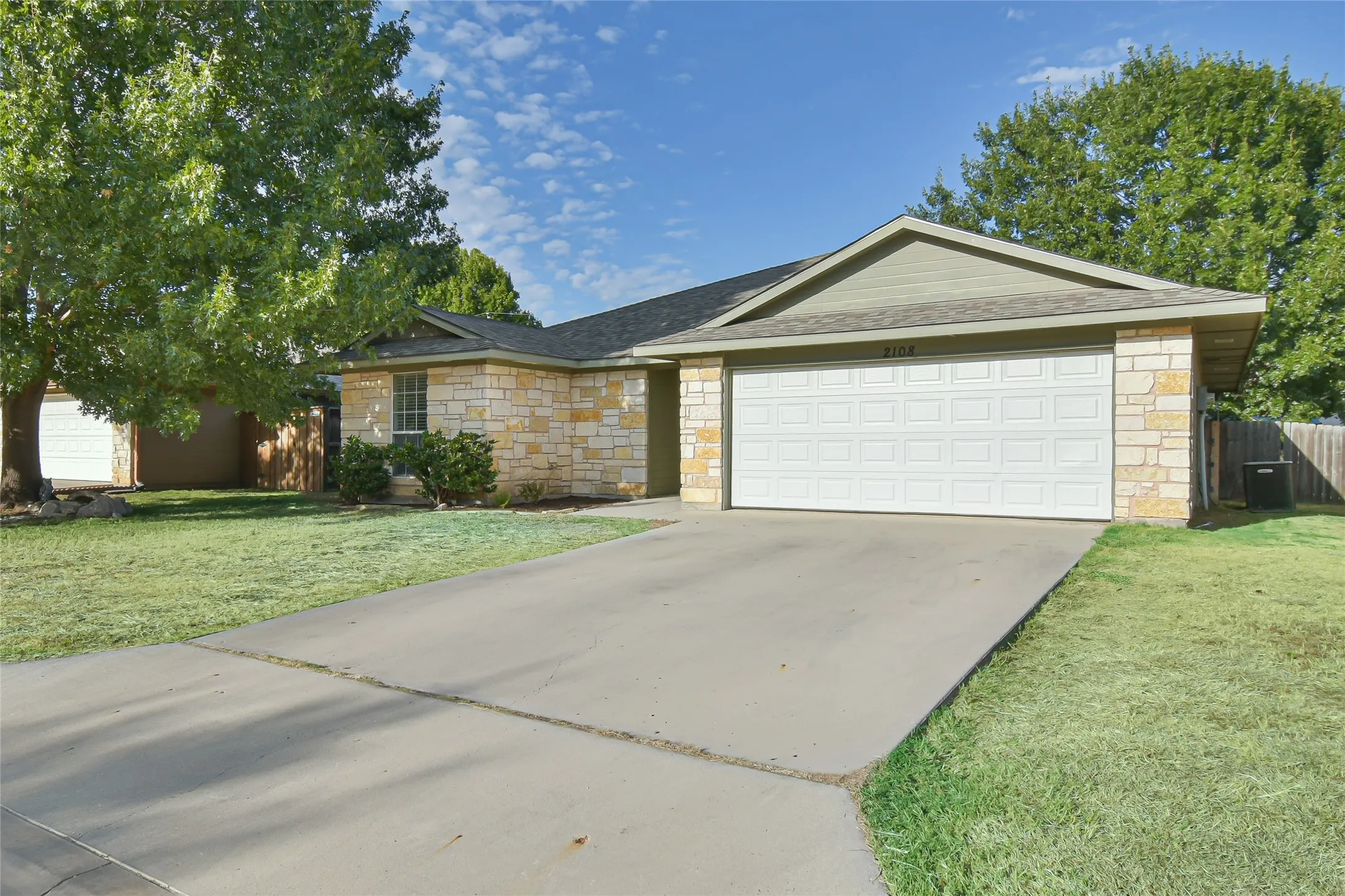 Stone facade, attached garage, concrete driveway, and mature landscaping