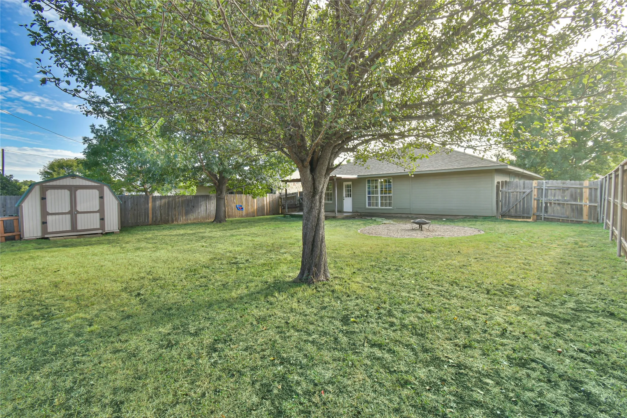 Expansive backyard featuring a mature tree, wood fencing, and a storage shed