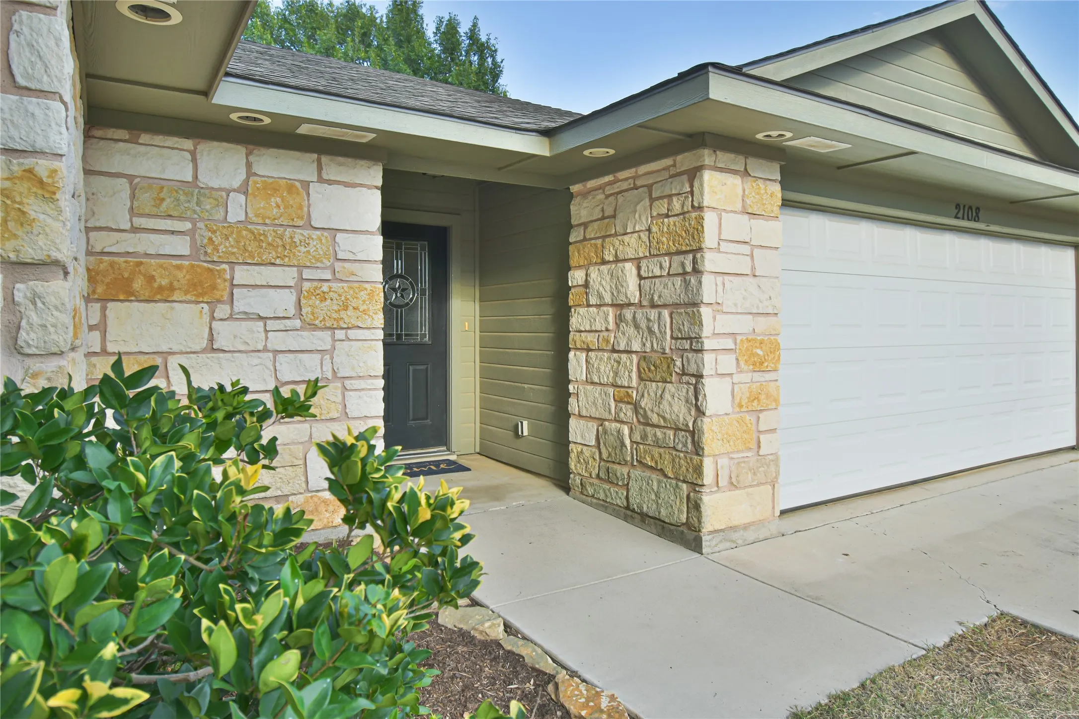 Stone veneer facade, recessed lighting, covered entry, front door with decorative glass, and a paneled garage door