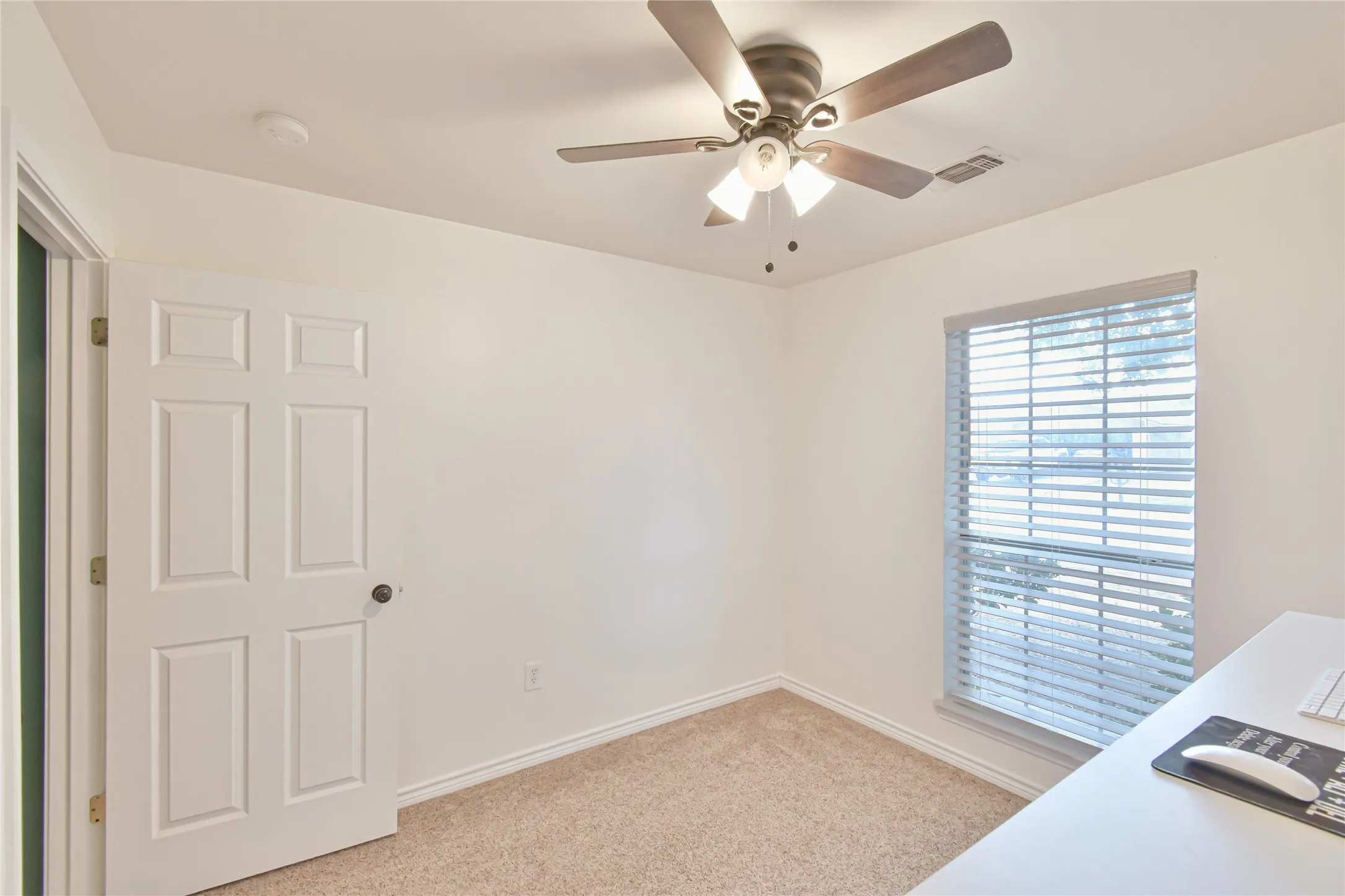 Neutral wall paint, textured carpeting, window with blinds, ceiling fan with integrated lighting, and a paneled interior door