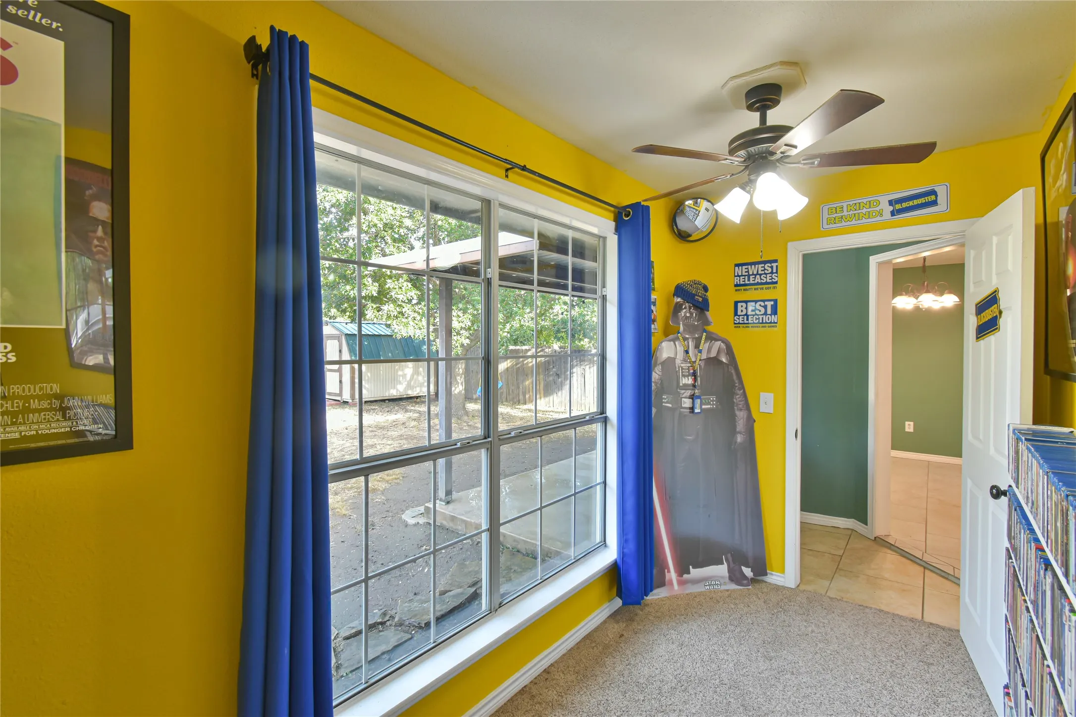 Carpeted room with a multi-pane window, ceiling fan with light fixture, and a white paneled door