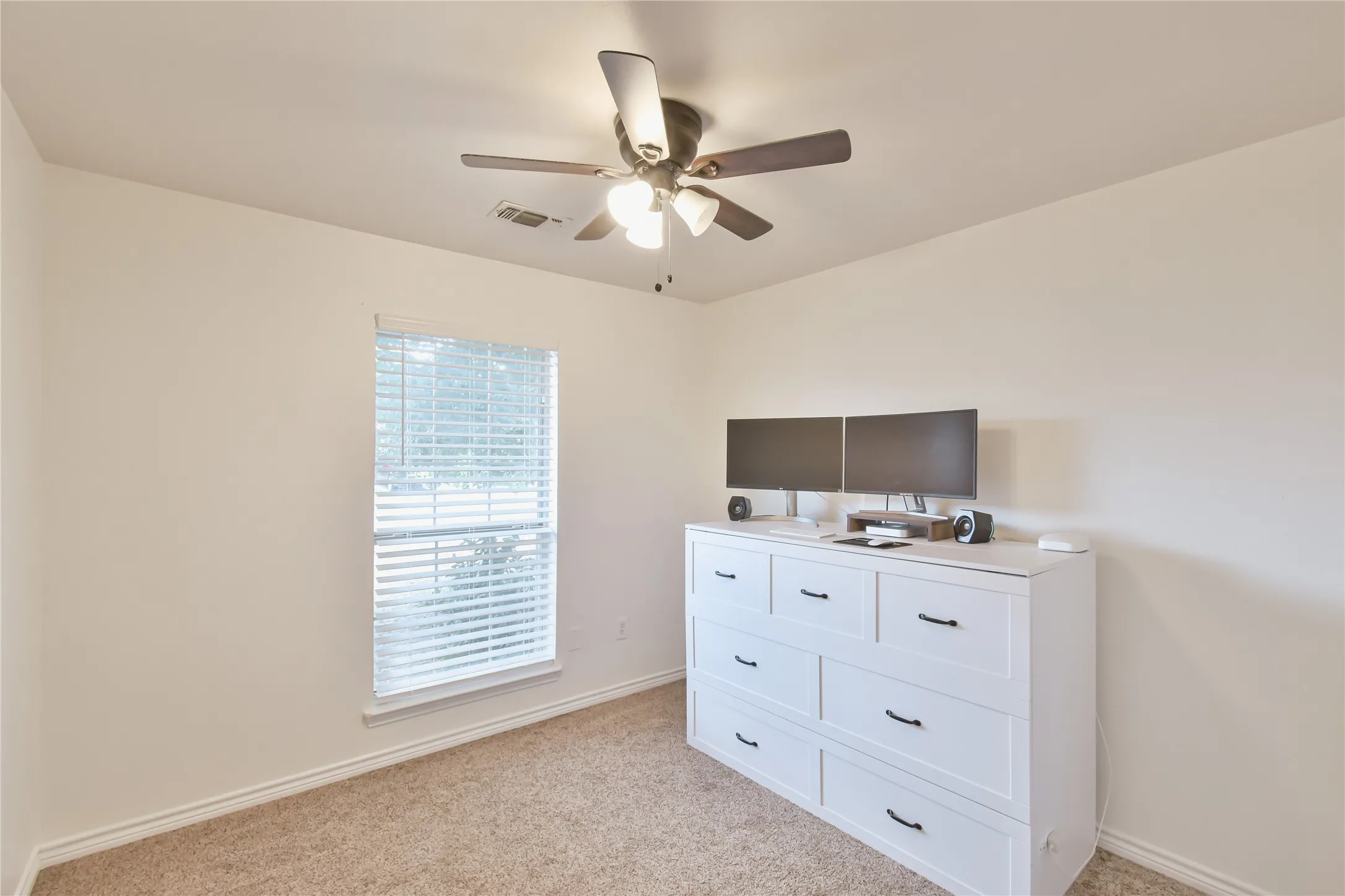 Neutral wall color, ceiling fan with integrated lighting, window with horizontal blinds, and carpeted flooring