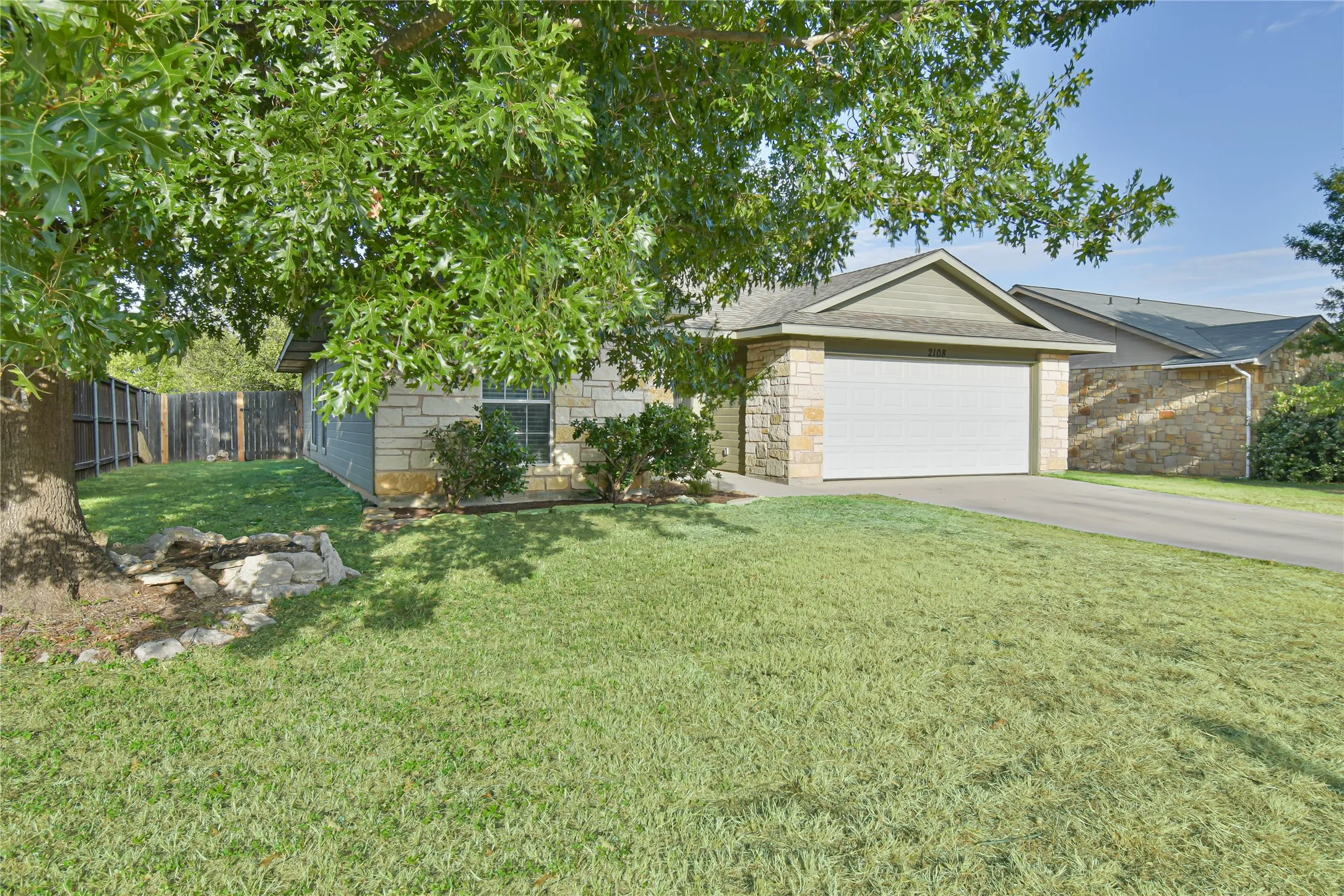 Stone veneer exterior with an attached garage, pitched roof, paved driveway, and established front lawn
