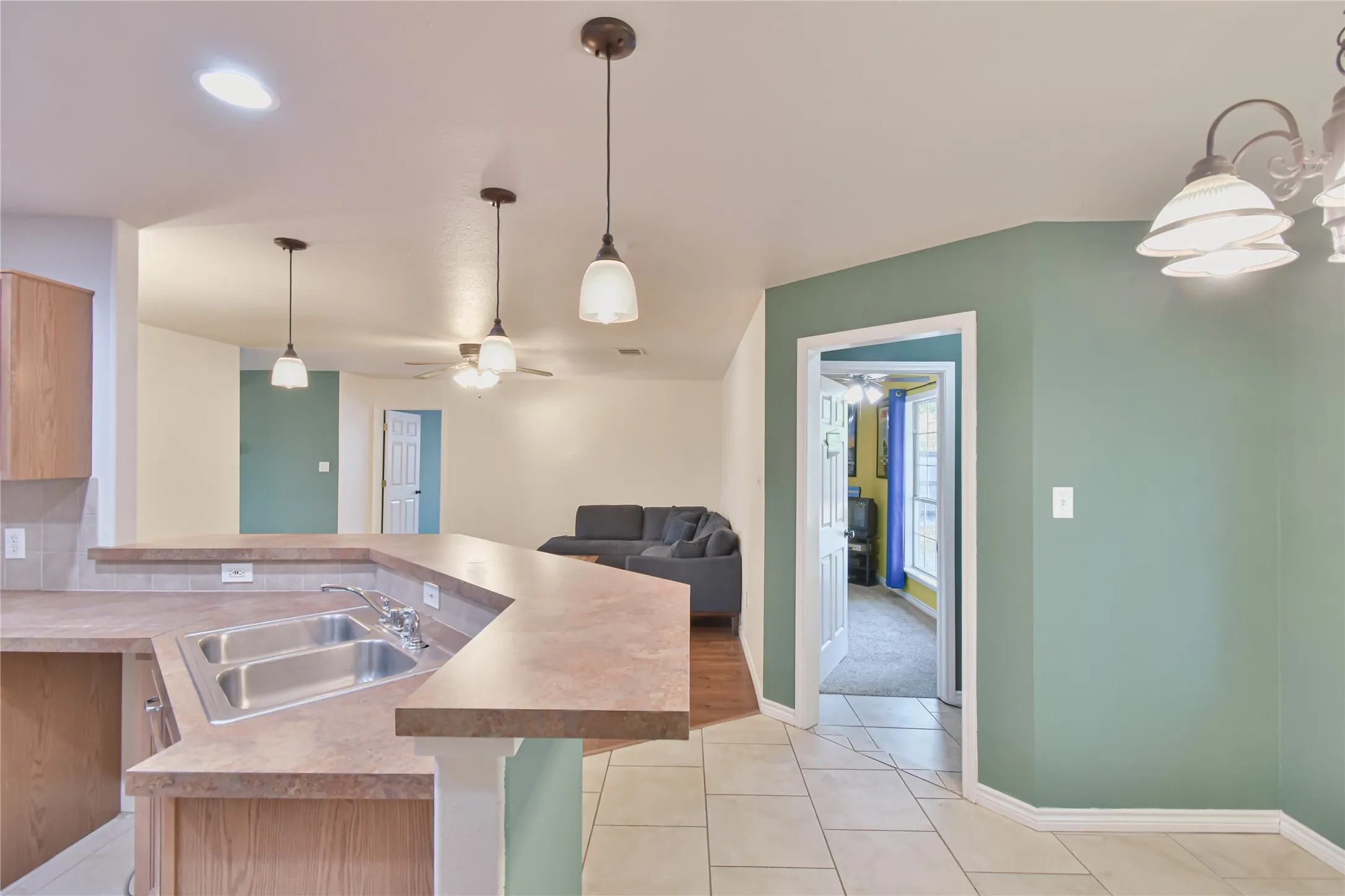 Kitchen island with a double basin stainless steel sink, laminate countertops, recessed lighting, and pendant lighting