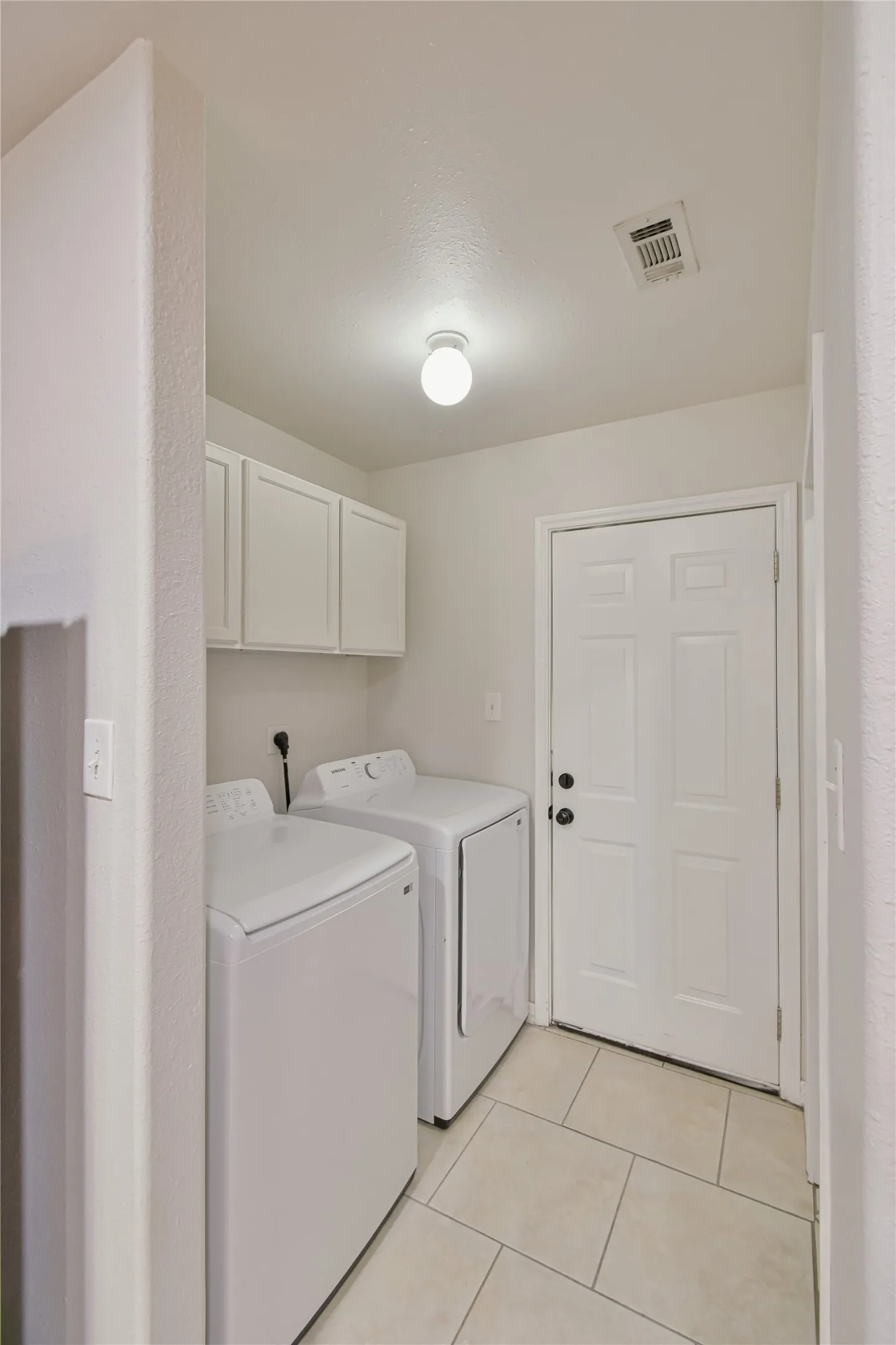 Laundry area with ceiling-mounted light fixture, upper cabinetry, and tile flooring