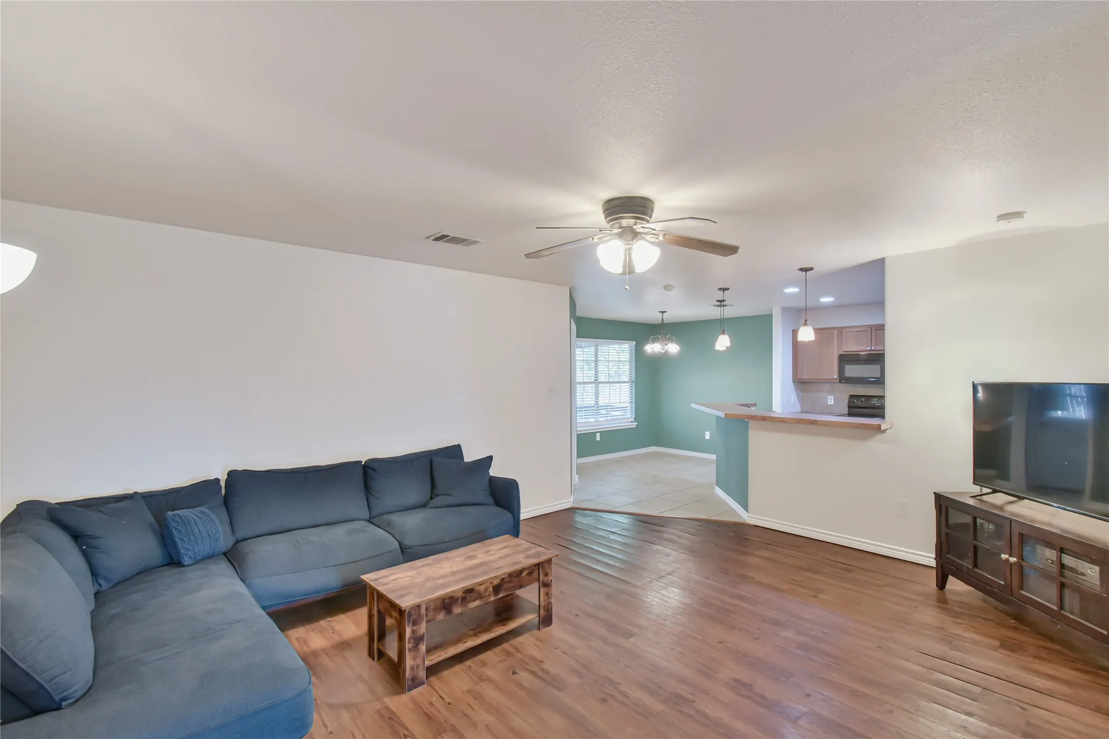 Expansive living area with wood-finish flooring, a ceiling fan, and recessed lighting