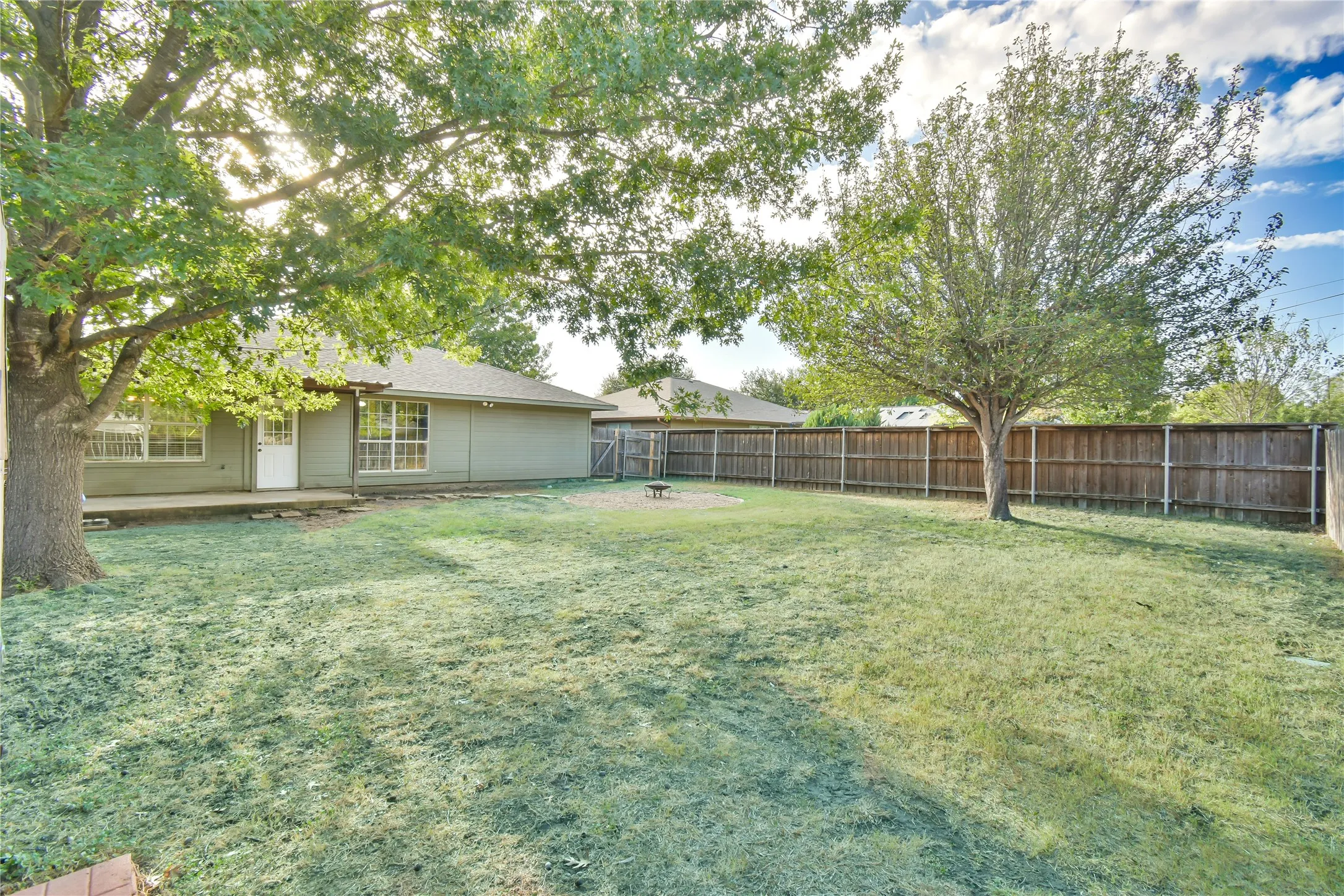 Expansive backyard featuring a large tree, wooden privacy fencing, and a concrete patio