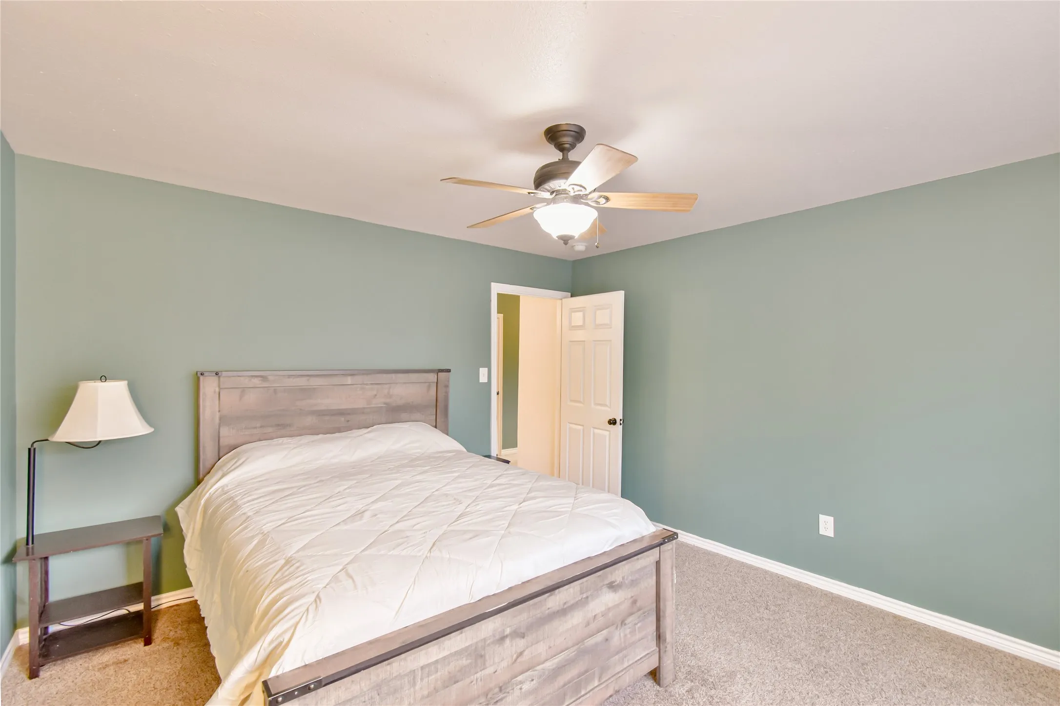 Light gray-green wall paint, carpet flooring, white trim, and a ceiling fan with integrated lighting