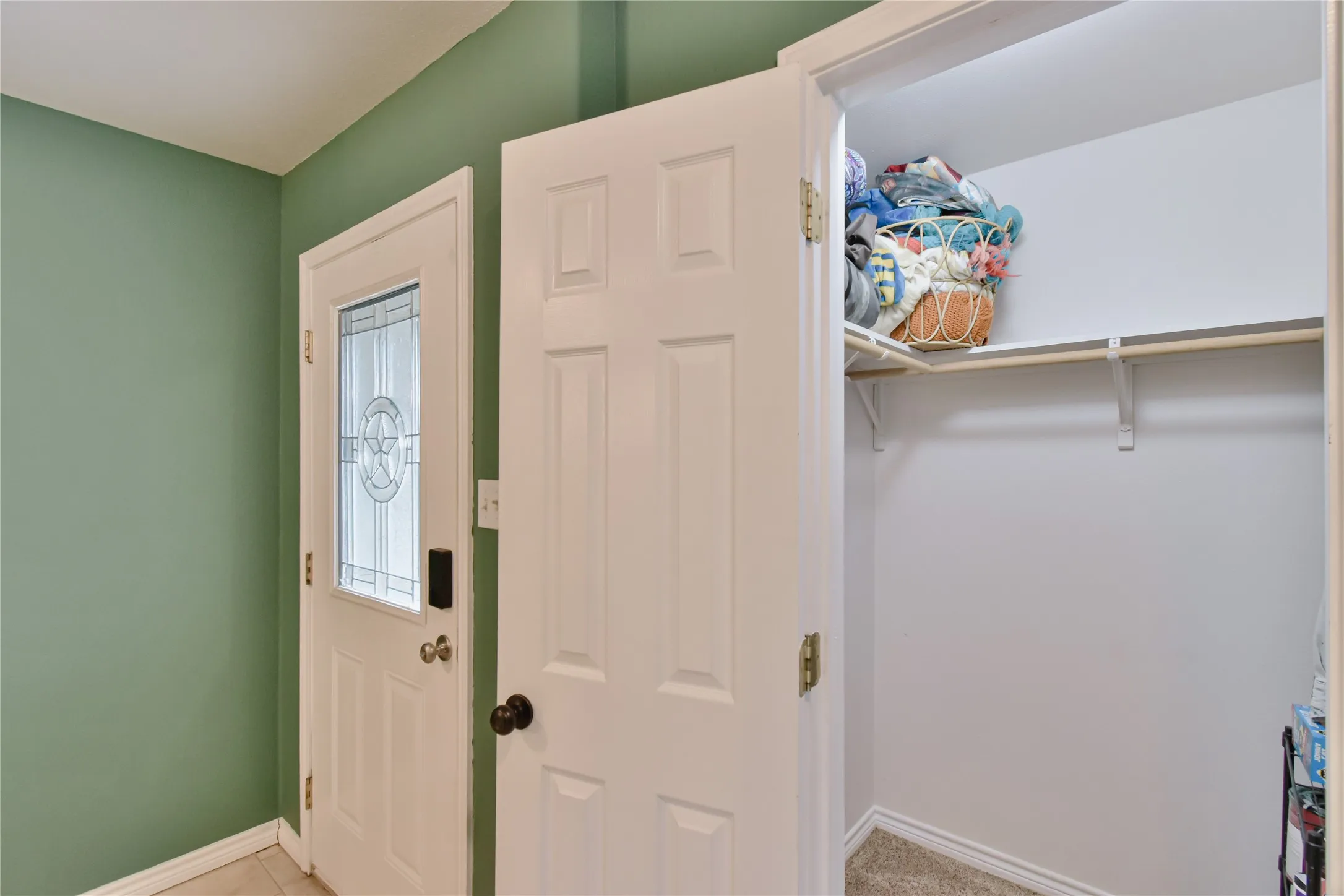 Entryway featuring a white paneled door with decorative glass, a white six-panel interior door, and a built-in closet with shelving and a hanging rod