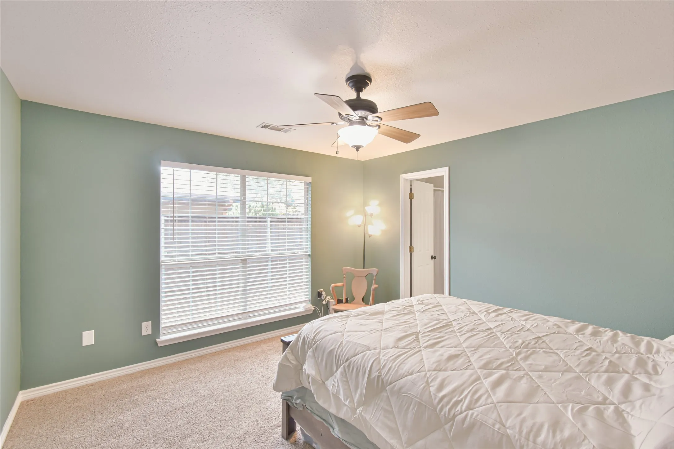Recessed ceiling, neutral carpet, large window with blinds, ceiling fan with integrated lighting, and a white door frame