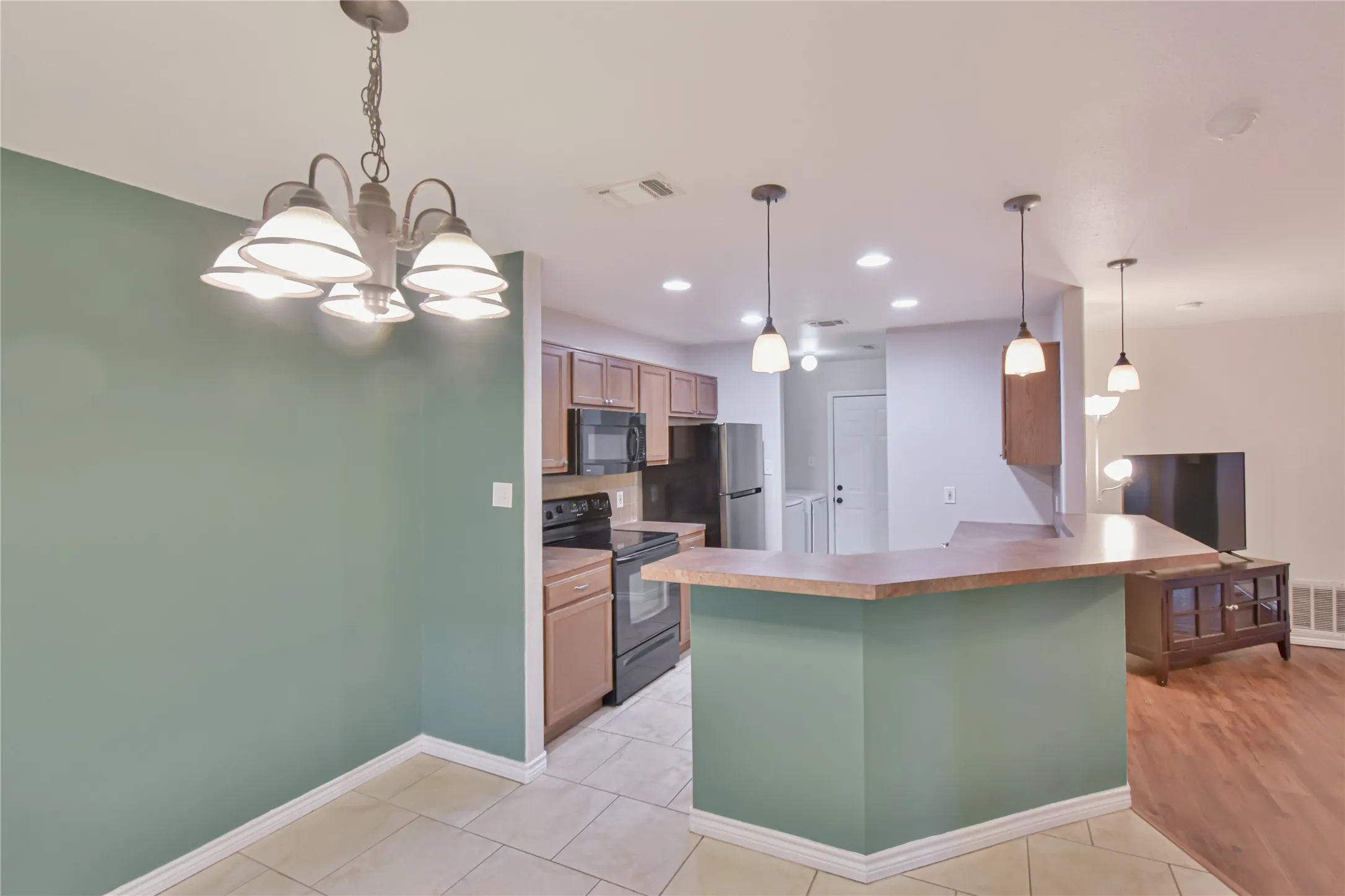 Kitchen featuring wood-finish cabinetry, black appliances, and a breakfast bar with pendant lighting