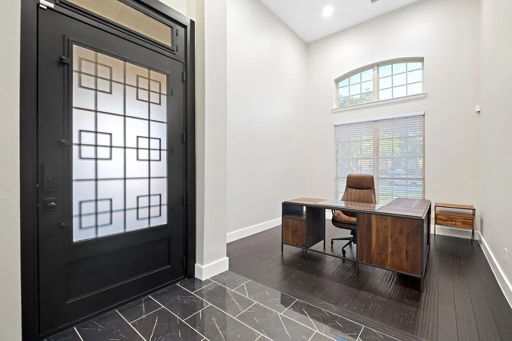 Black iron front door with frosted glass panels, dark tile entry, dark wood-finish flooring, high ceilings, and arched transom window