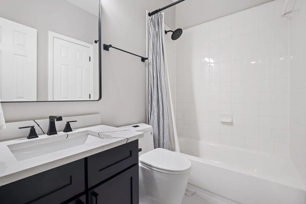 White subway tile bath surround, black vanity with integrated sink, black matte faucet, rectangular framed mirror, and a black matte shower head
