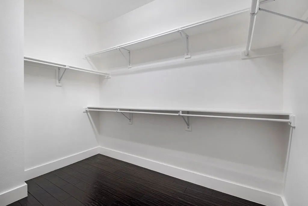 Spacious closet featuring multiple white shelving units, white hanging rods, and dark wood-finish flooring
