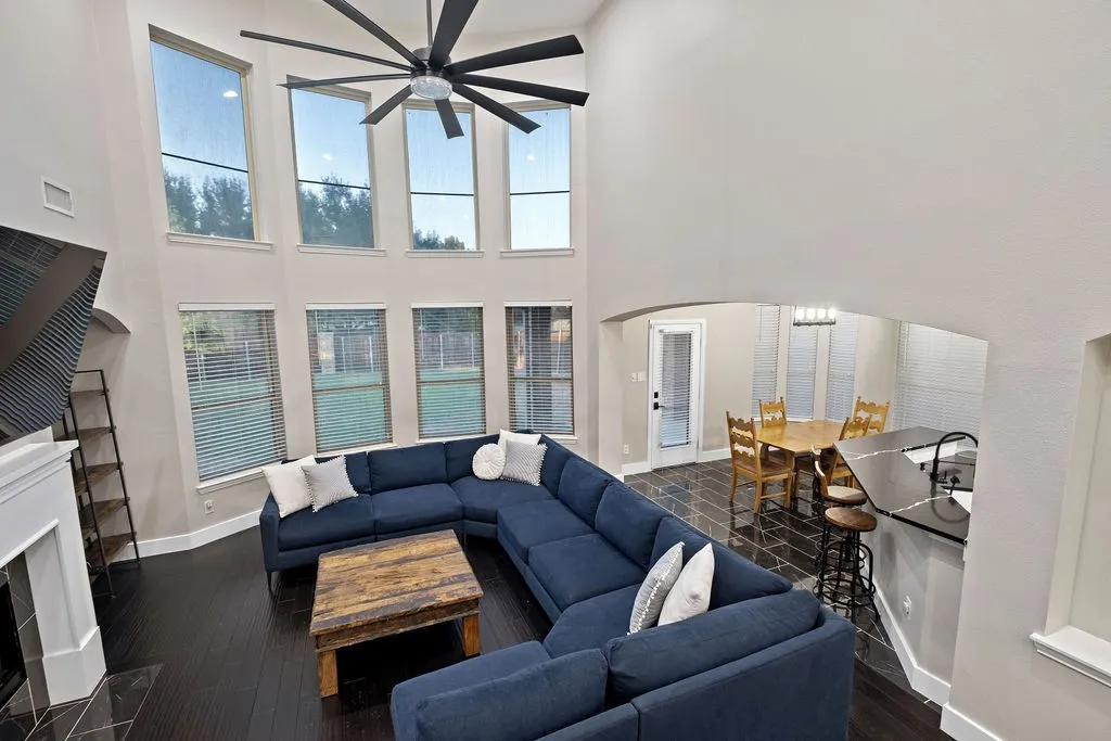 Two-story living area with dark wood-finish flooring, a contemporary ceiling fan, and multiple windows