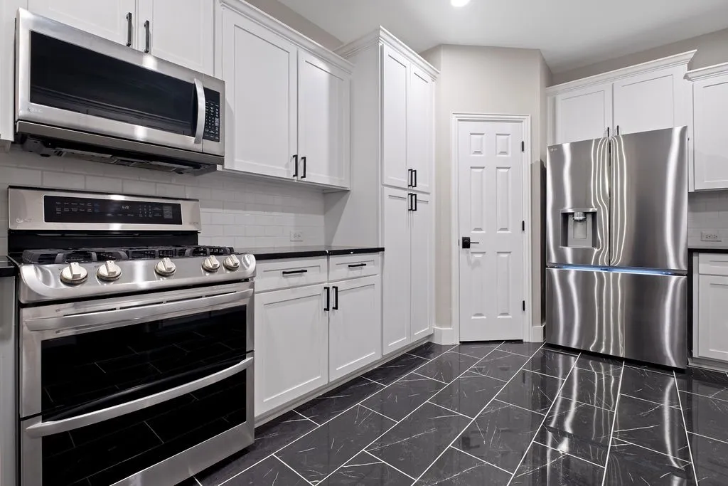 Stainless steel appliances, white shaker cabinetry, dark countertops, subway tile backsplash, and dark tile flooring