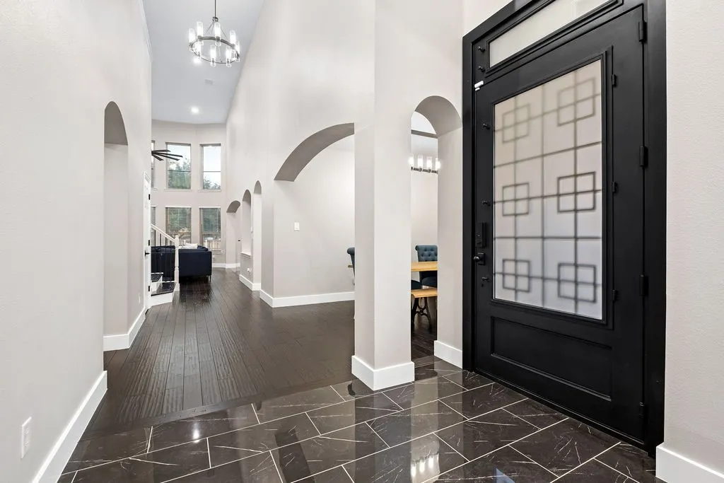 Black entry door with frosted glass detailing, glossy dark tile flooring, arched doorways, wood-finish flooring, and a chandelier lighting fixture