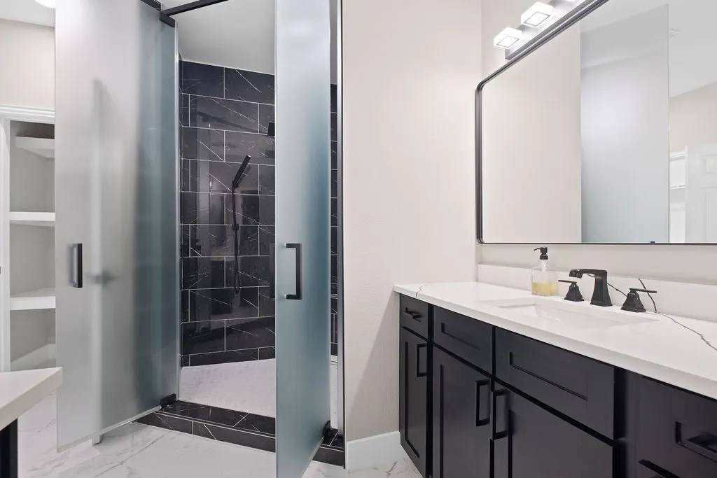 Frosted glass shower enclosure, black tiled shower walls, black vanity cabinetry, white countertop, and matte black plumbing fixtures