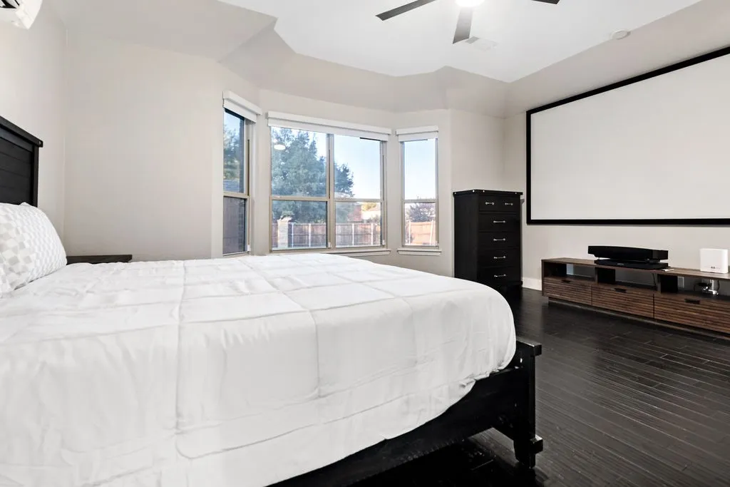 Dark wood-finish flooring with a ceiling fan light fixture, bay window, and built-in projection screen