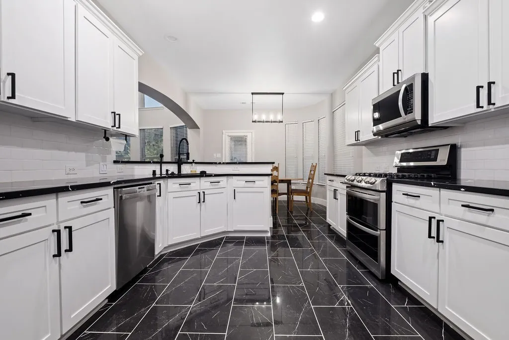 Well-appointed kitchen featuring white cabinetry, black countertops, stainless steel appliances, a subway tile backsplash, and a large format tile floor