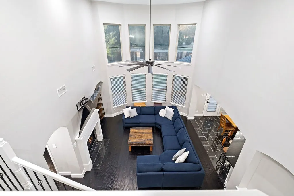 Two-story living area with dark wood-finish flooring, a white mantel fireplace, and a large ceiling fan