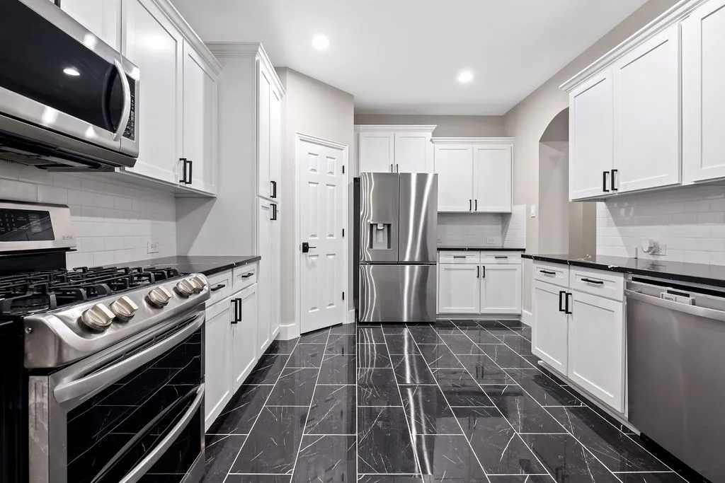 Kitchen featuring white shaker-style cabinetry, dark countertops, a white subway tile backsplash, stainless steel appliances, and dark tile flooring