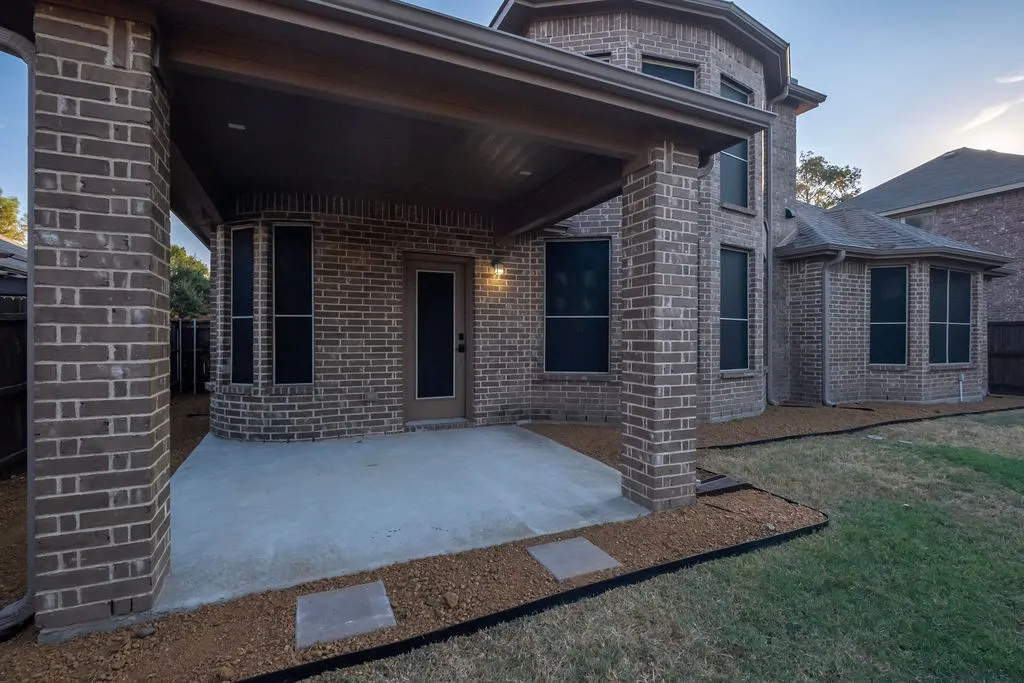 Brick exterior with a covered concrete patio, featuring a built-in outdoor light fixture, a door with a screen, and multiple windows