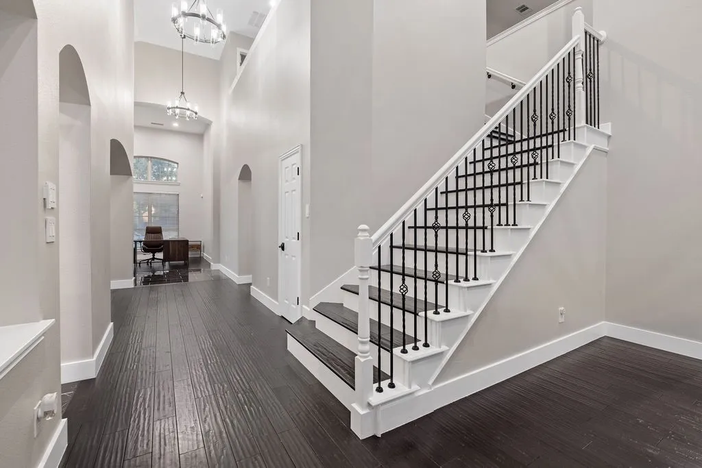 Grand entry hall featuring high ceilings, wood-finish flooring, a prominent staircase with decorative iron balusters, and arched doorways
