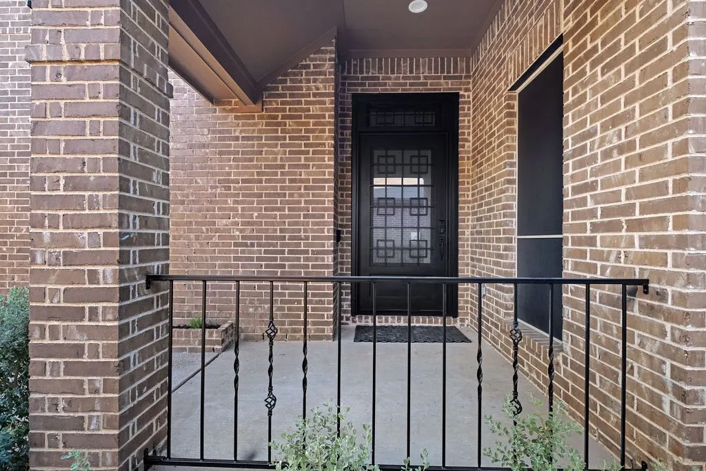 Brick exterior with a covered porch, decorative wrought iron railing, and a black front door with geometric glass inserts