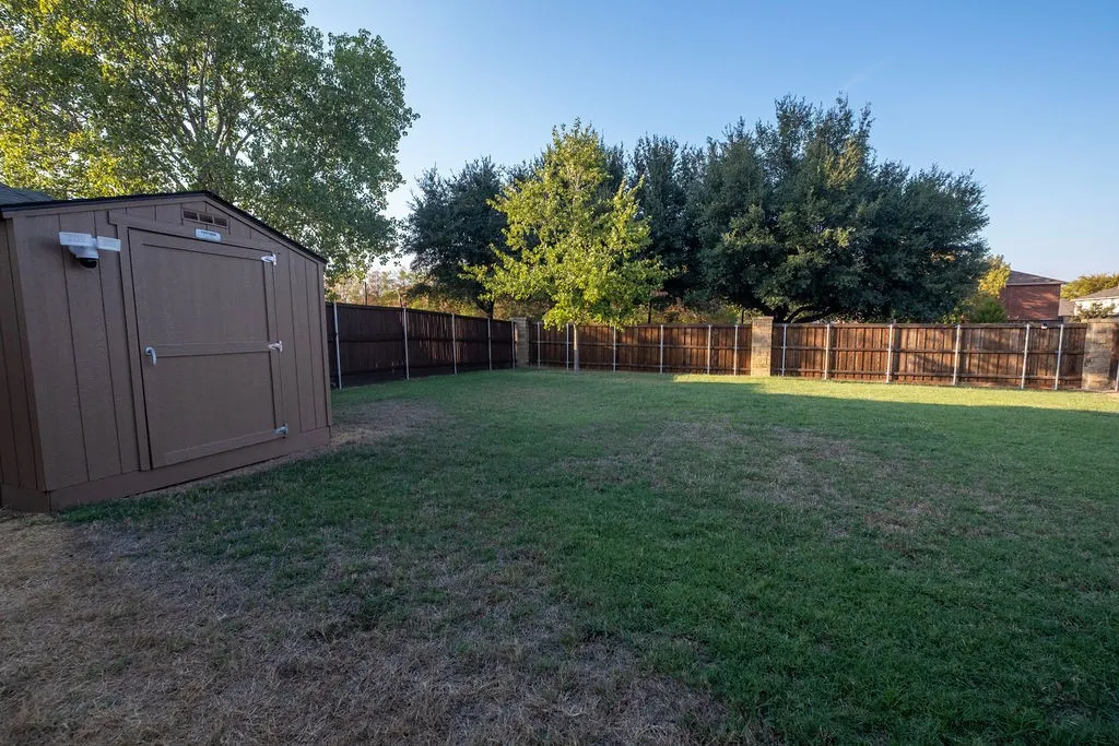 Expansive lawn area with a brown privacy fence, mature trees, and a functional storage shed