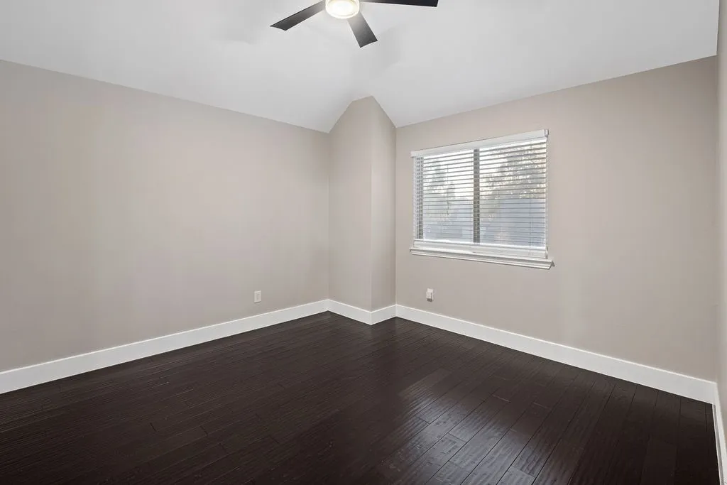 Vaulted ceiling with an attached ceiling fan, dark wood-finish flooring, and a window with horizontal blinds